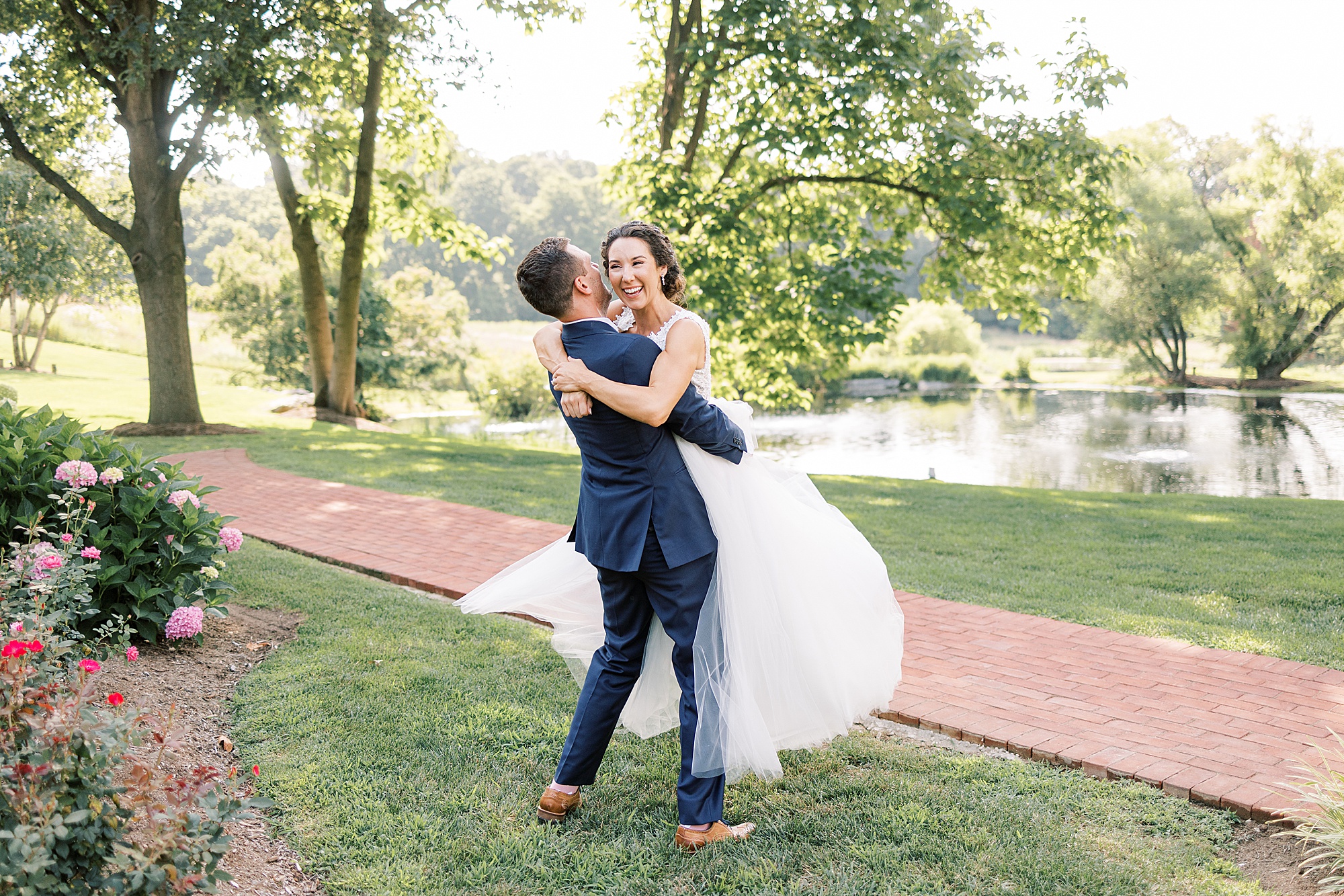 groom lifts bride twirling her around by pond at The Farm at Eagles Ridge 