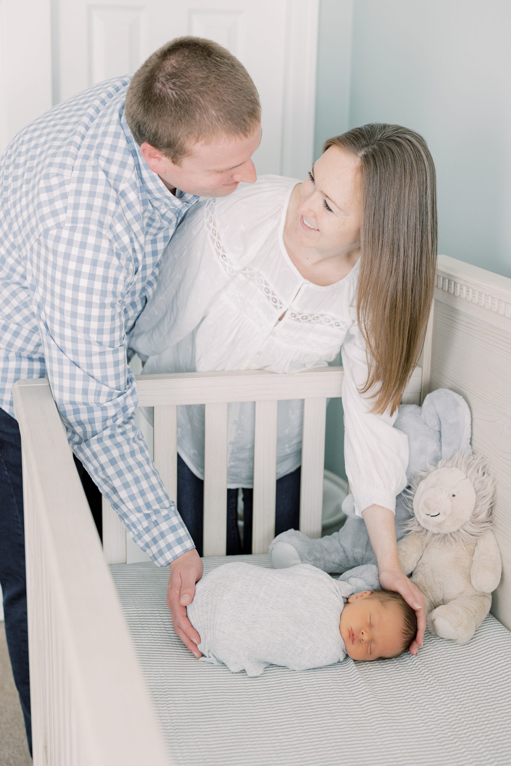mother and father cradling baby in neutral toned nursery crib 