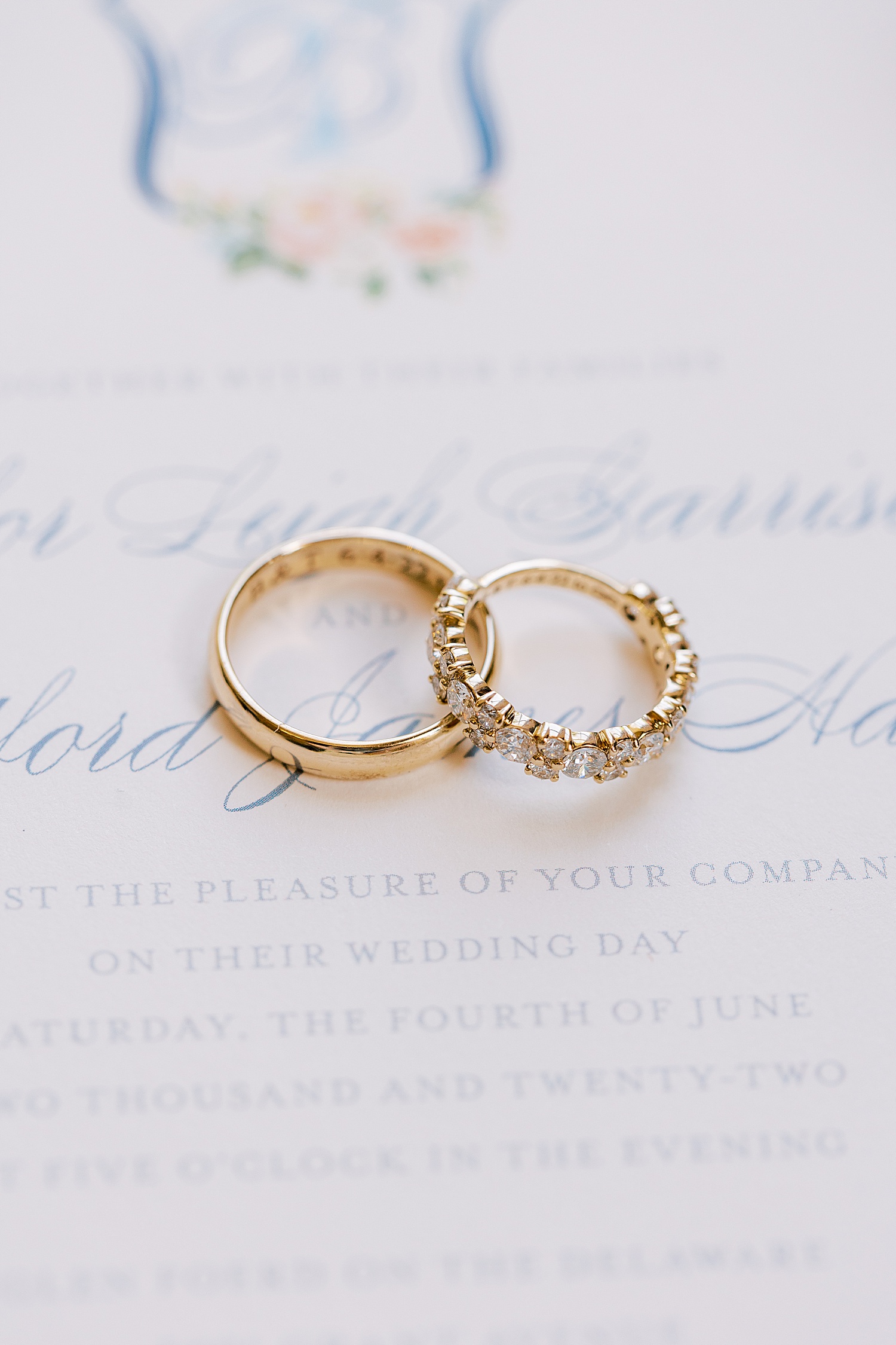gold wedding bands rest on invitation suite with blue script 