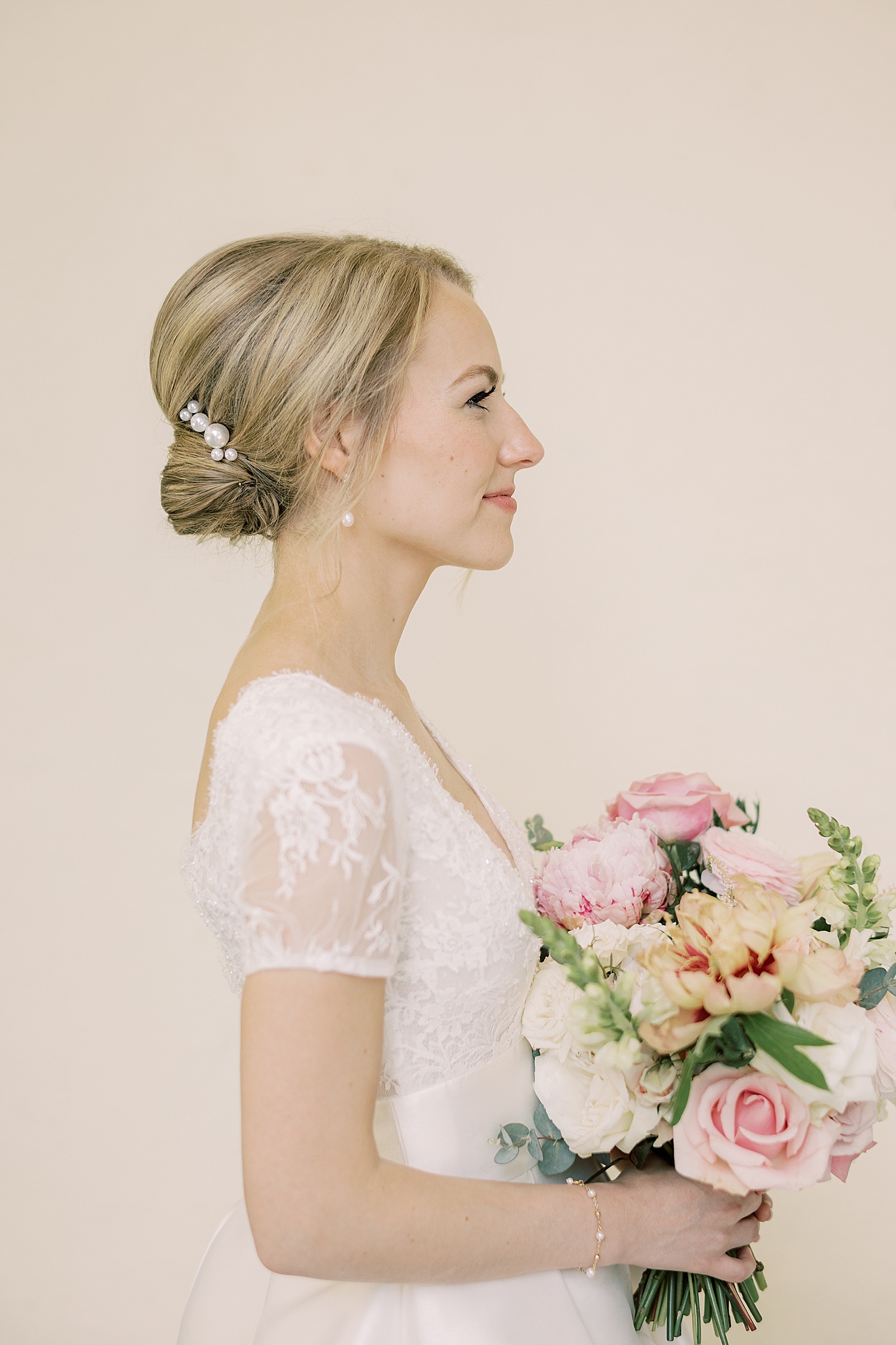 bride stands facing the right holding bouquet of pink peonies 