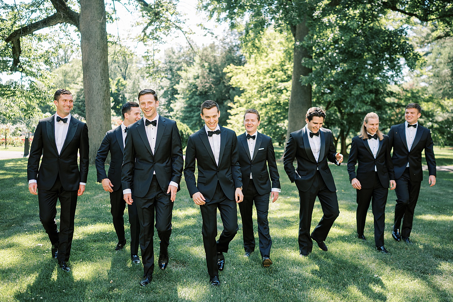 groom walks on lawn with groomsmen in classic suits at Glen Foerd on the Delaware