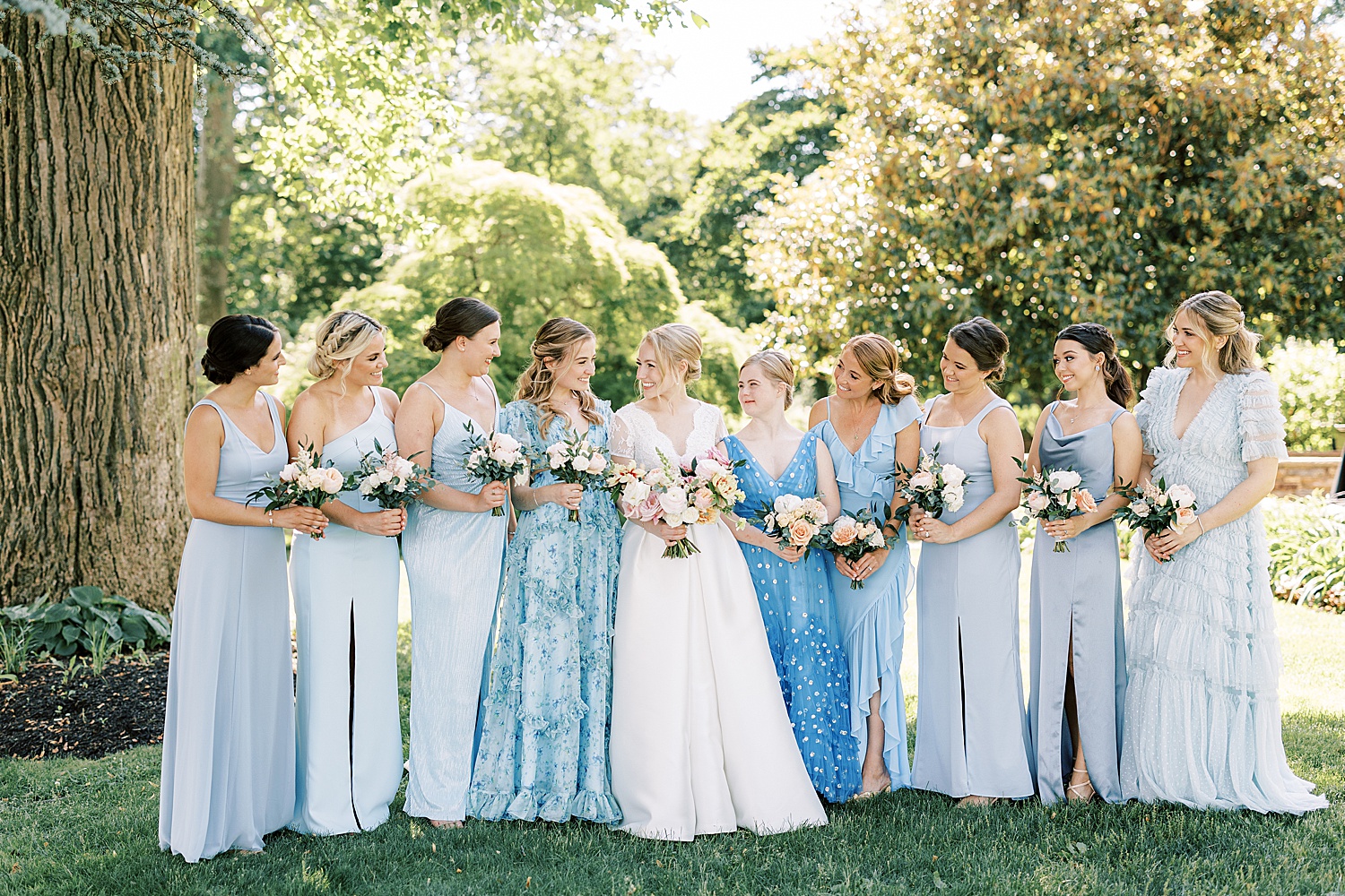 bride stands with 9 bridesmaids in mismatched blue gowns at Glen Foerd on the Delaware