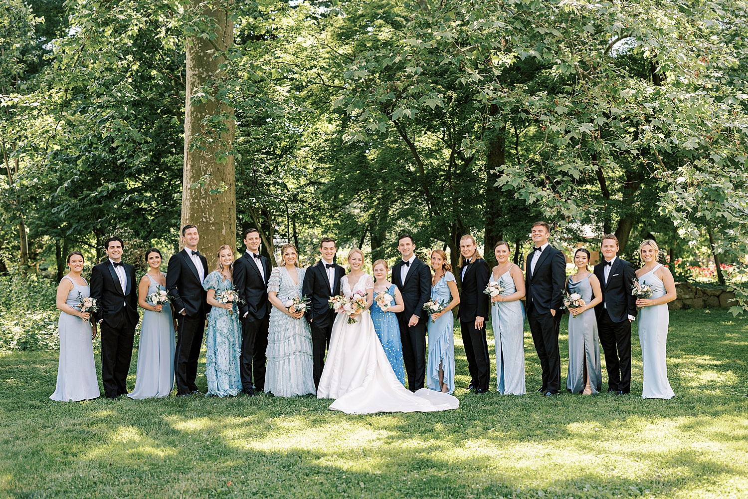 bride and groom pose with wedding party in classic suits and mismatched blue gowns at Glen Foerd on the Delaware