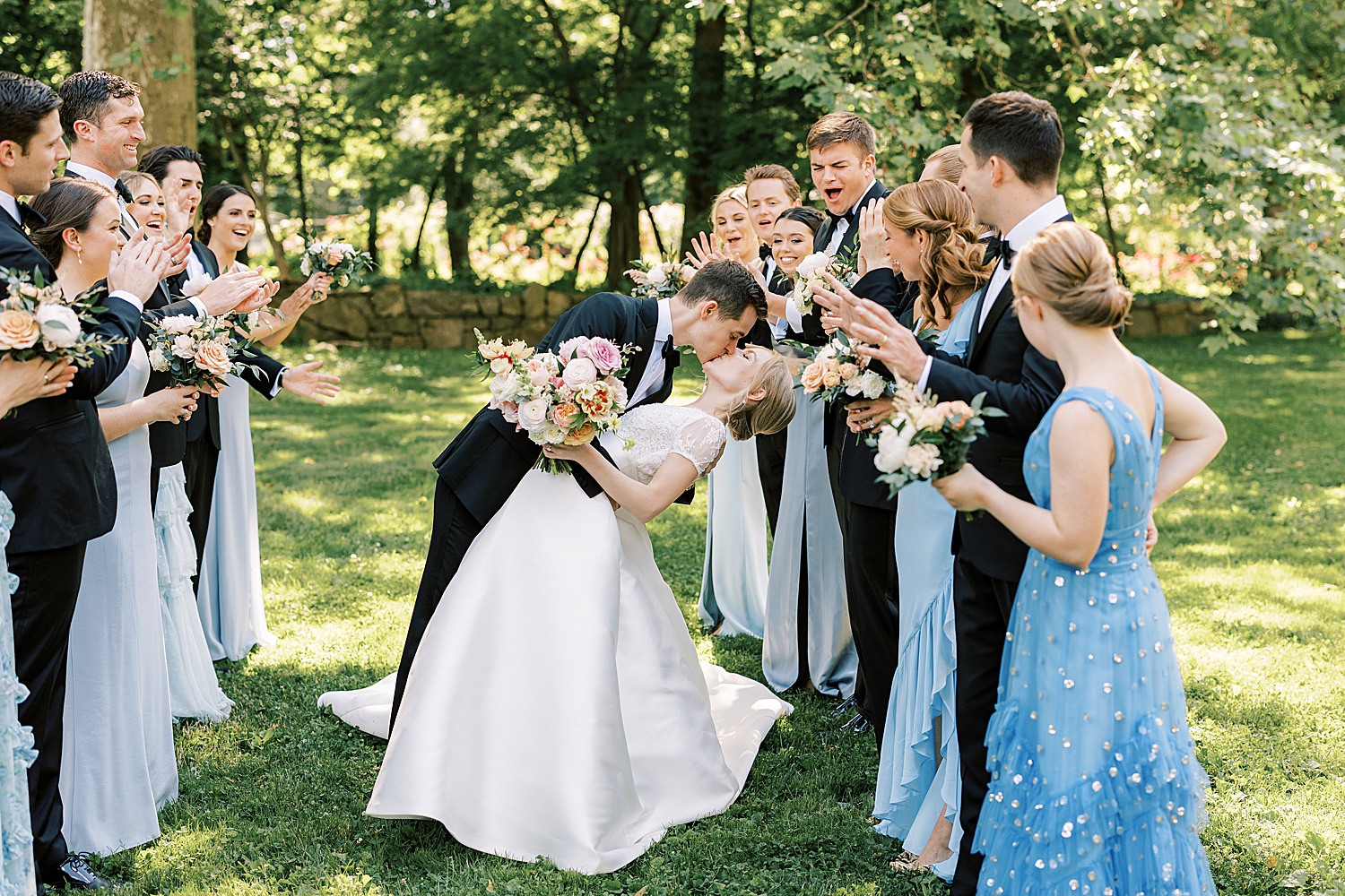 groom dips bride kissing her between wedding party cheering at Glen Foerd on the Delaware