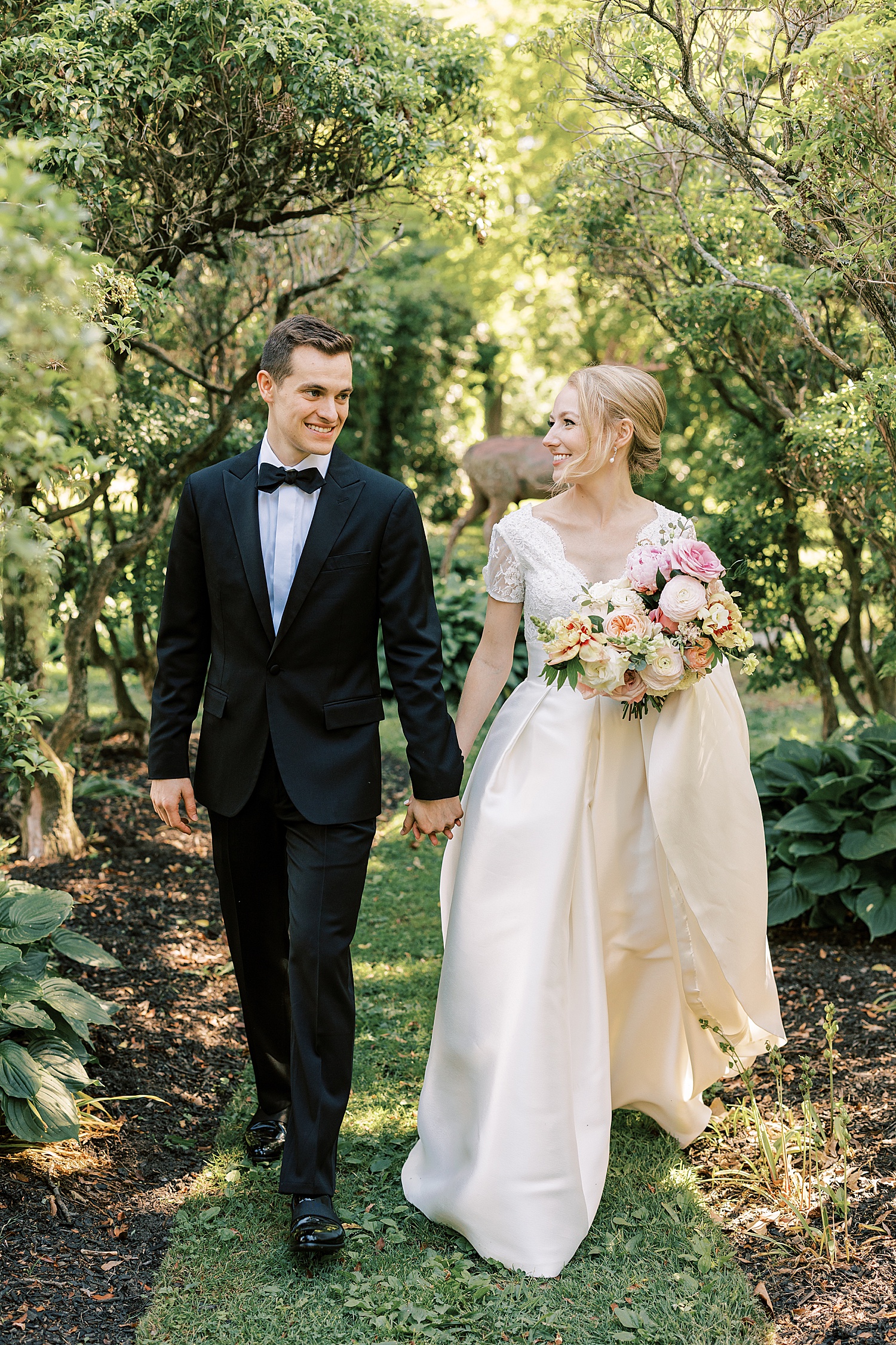 groom in black suit walks holding bride's hand in cap sleeve wedding gown 