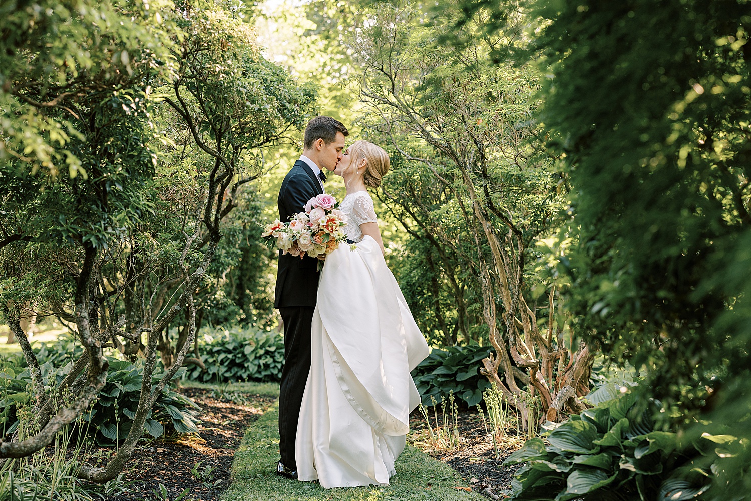 bride and groom kiss among trees in gardens at Glen Foerd on the Delaware