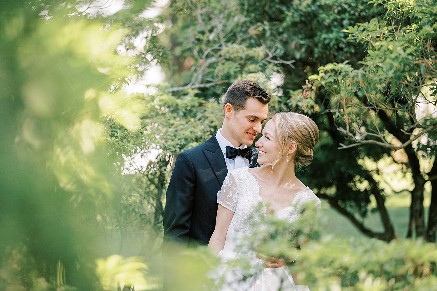 groom leans to whisper in bride's ear in gardens at Glen Foerd on the Delaware
