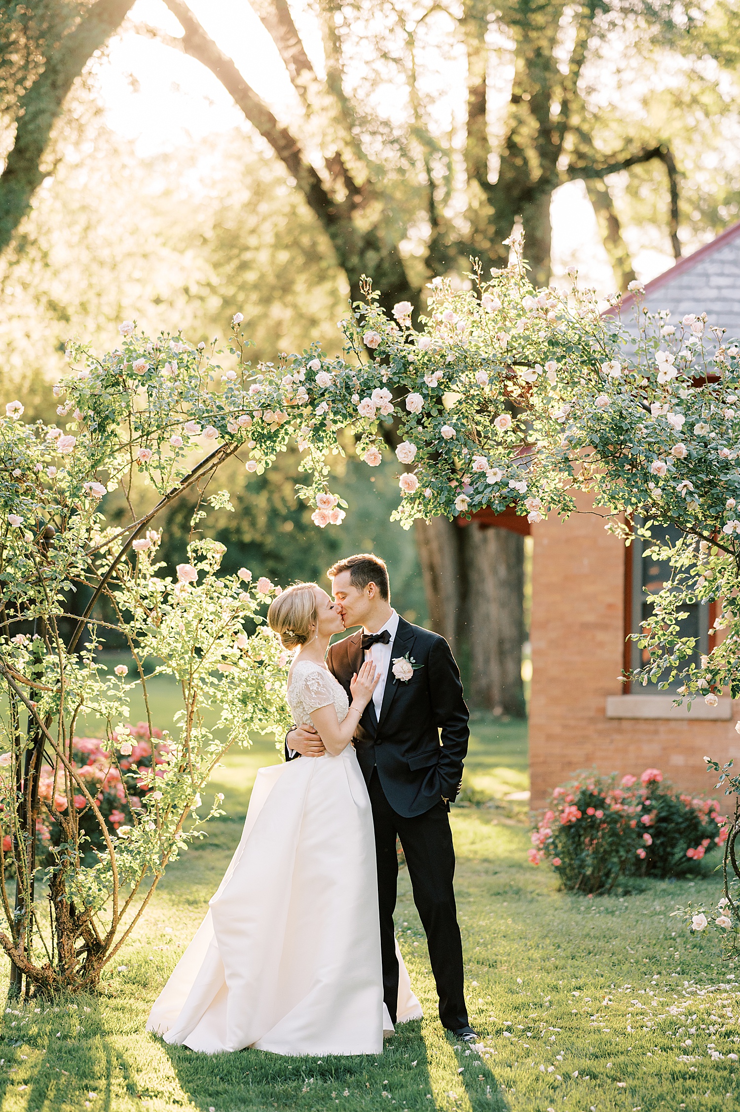 newlyweds kiss under pink roses in garden at Glen Foerd on the Delaware
