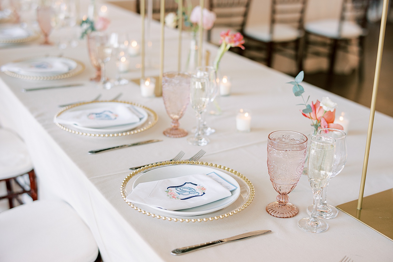 place setting with gold rimmed plates, pink depression glasses and custom crest napkins 