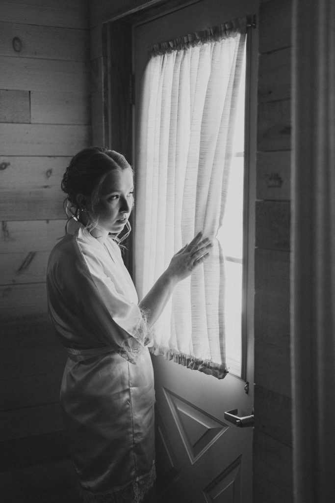 black and white photograph of bride peeking through window on her wedding day
