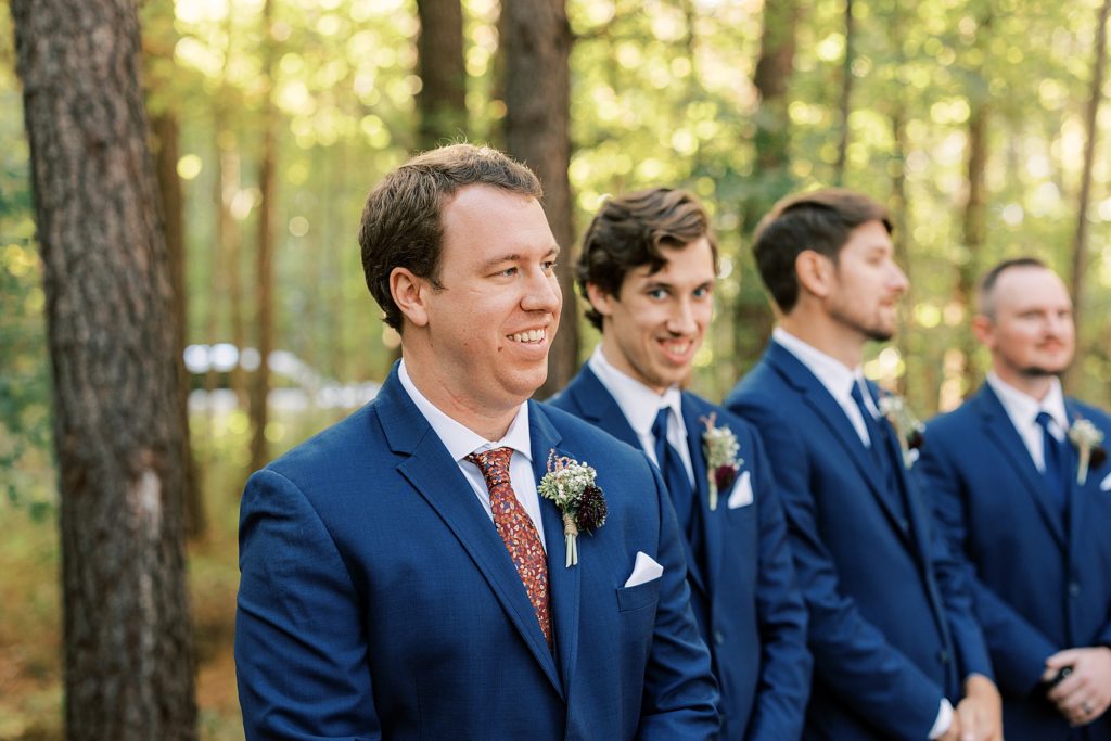groom watches his bride as she walks down the aisle with a huge smile on his face