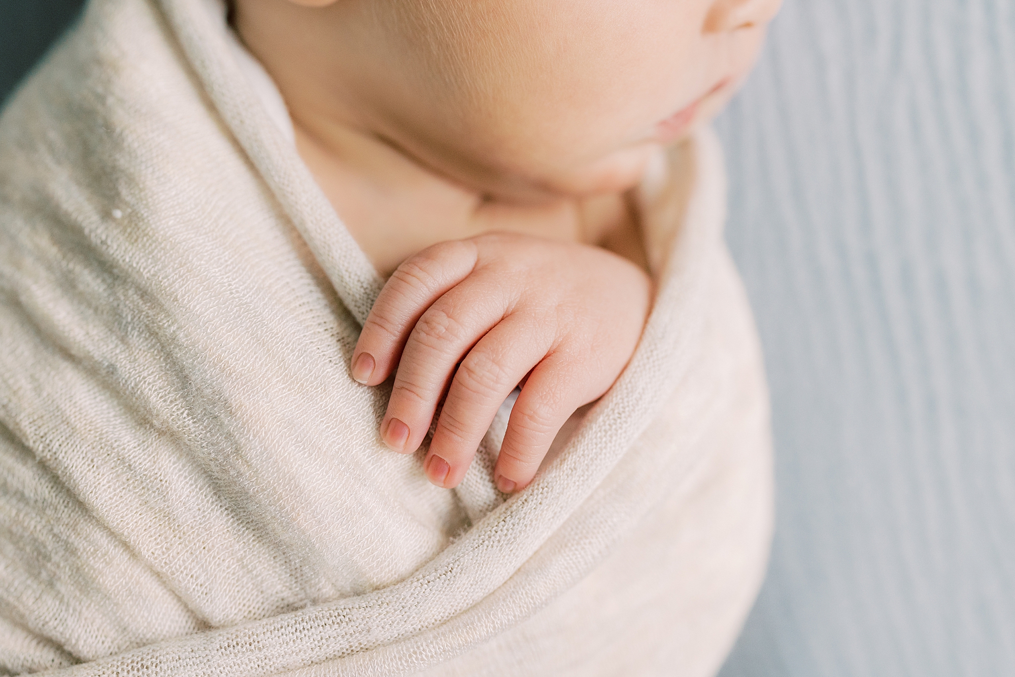 baby lays in white wrap on blue backdrop 