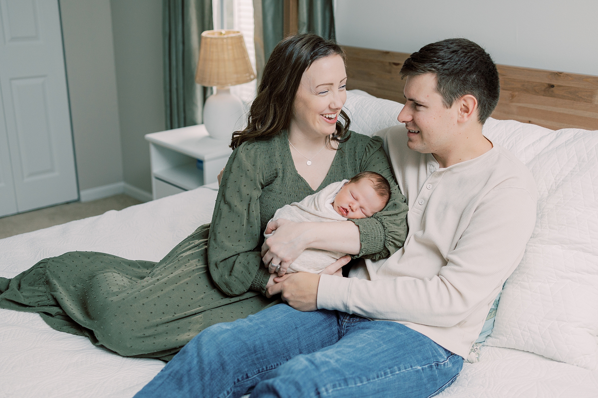 parents laugh sitting on bed with newborn son