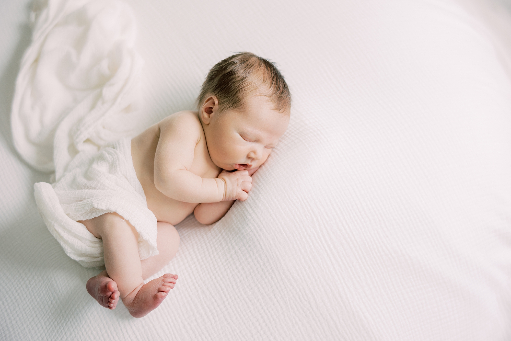 baby lays in white wrap during newborn photos on blanket 