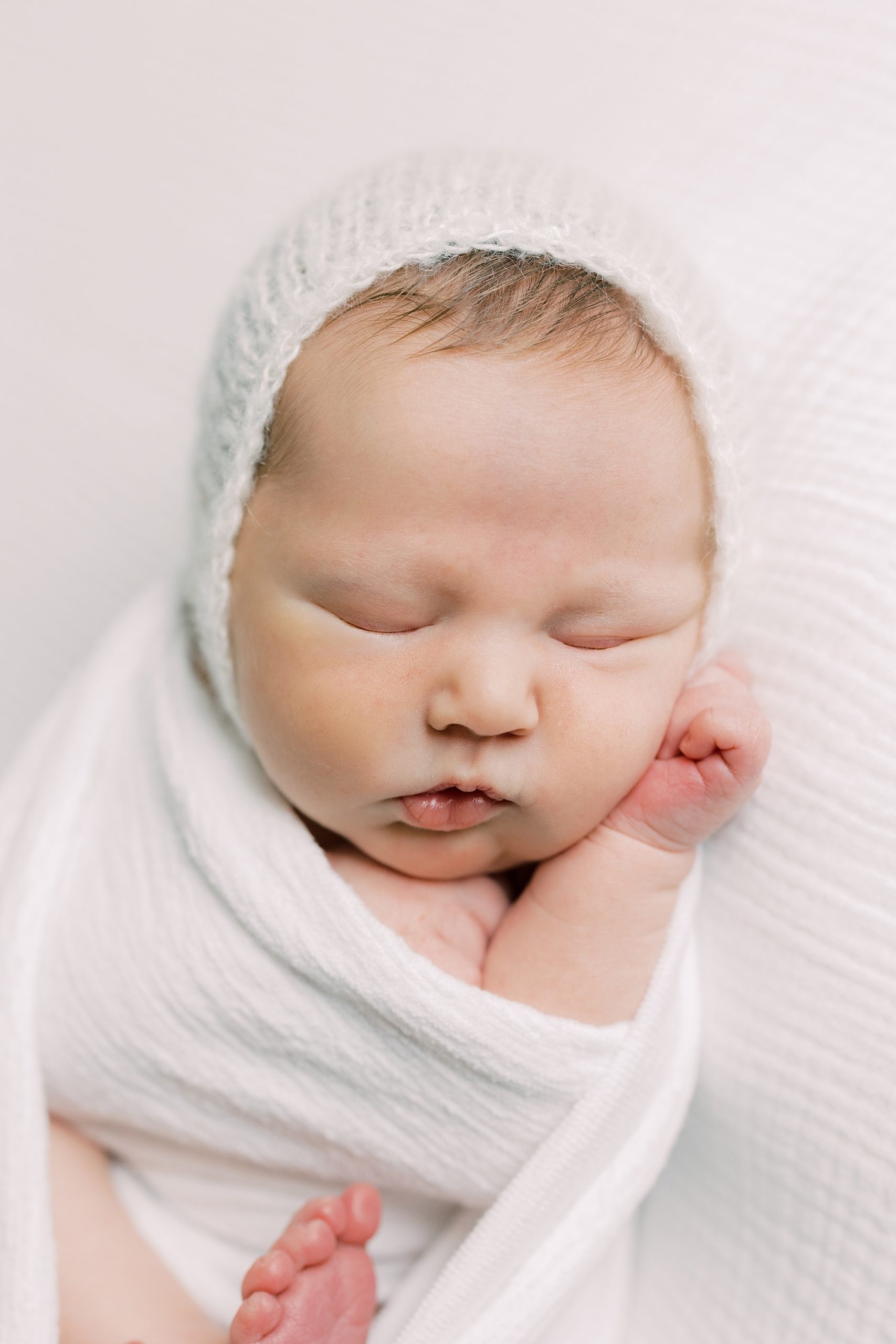 baby sleeps in white wrap with white bonnet