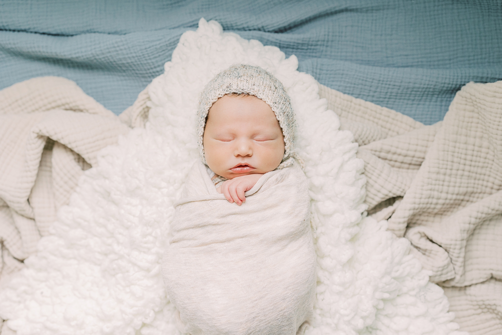 baby lays in white wrap on fluffy white blanket 