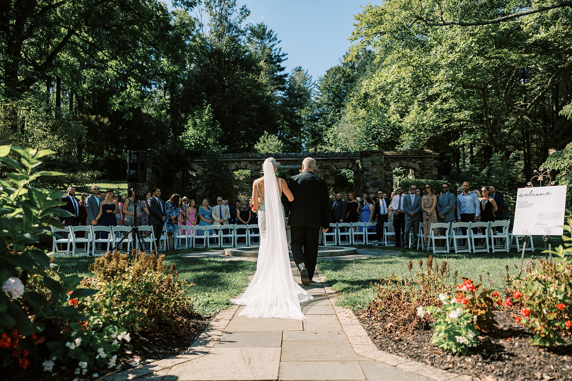 bride and father walk into summer wedding ceremony in gardens