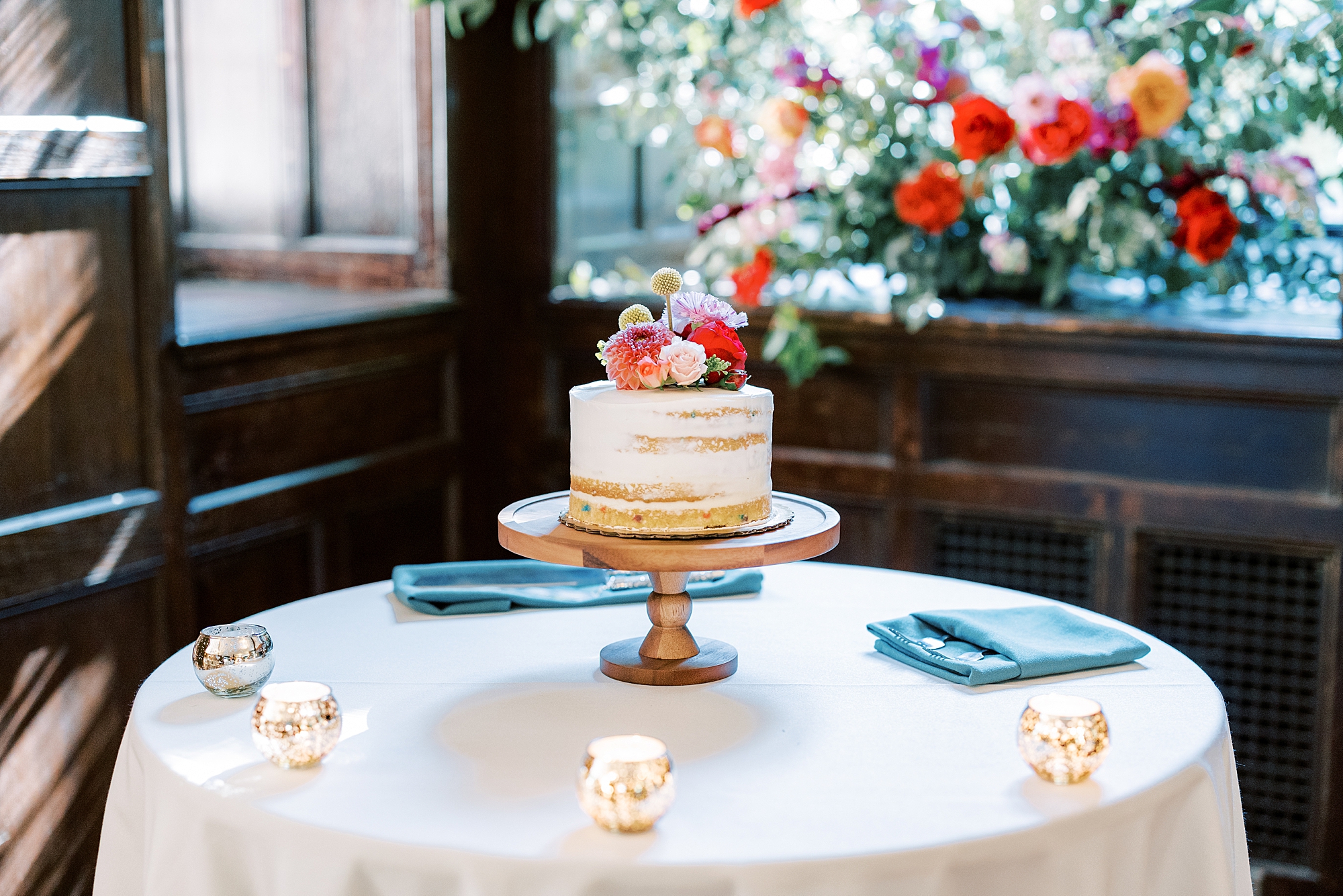 wedding cake sits in middle of table with teal napkins 