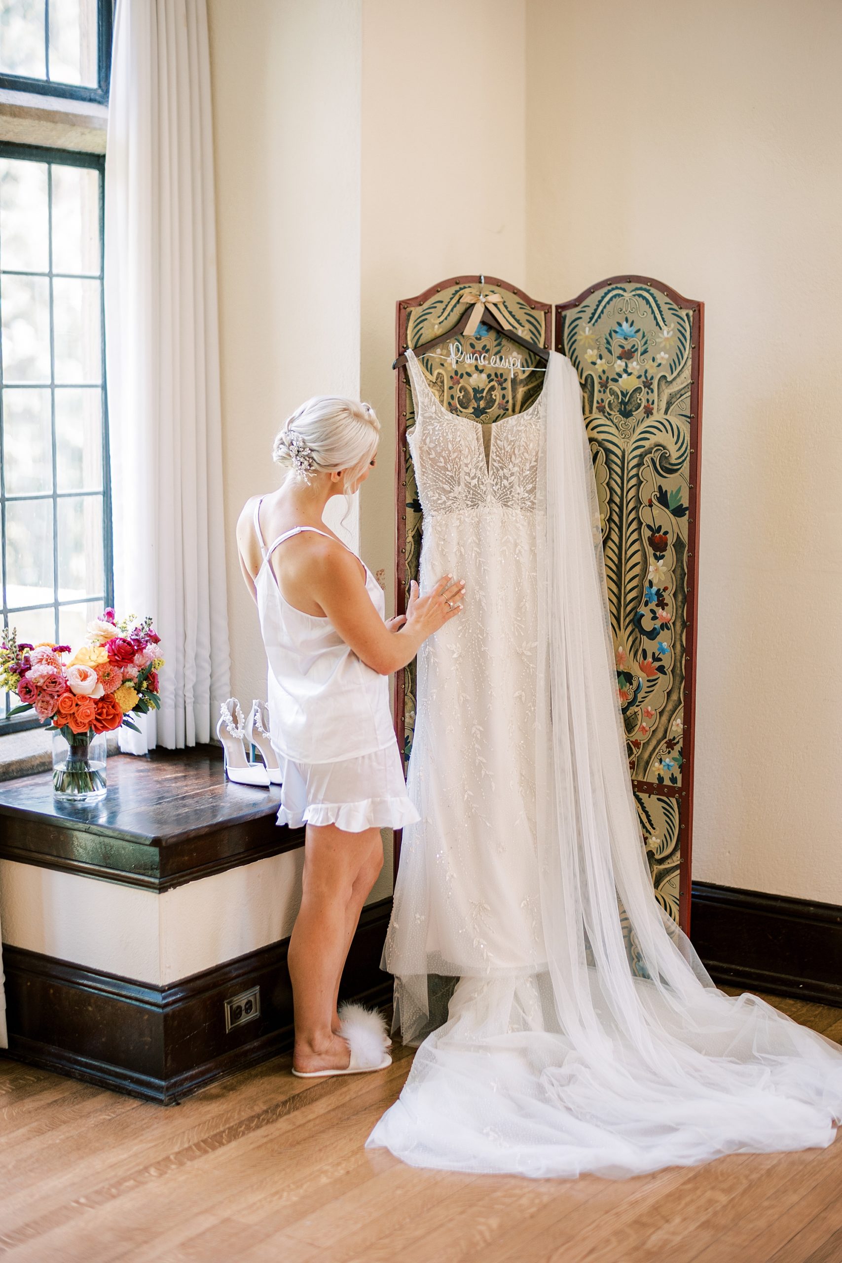 bride looks at wedding gown hanging on changing divider at Parque Ridley Creek