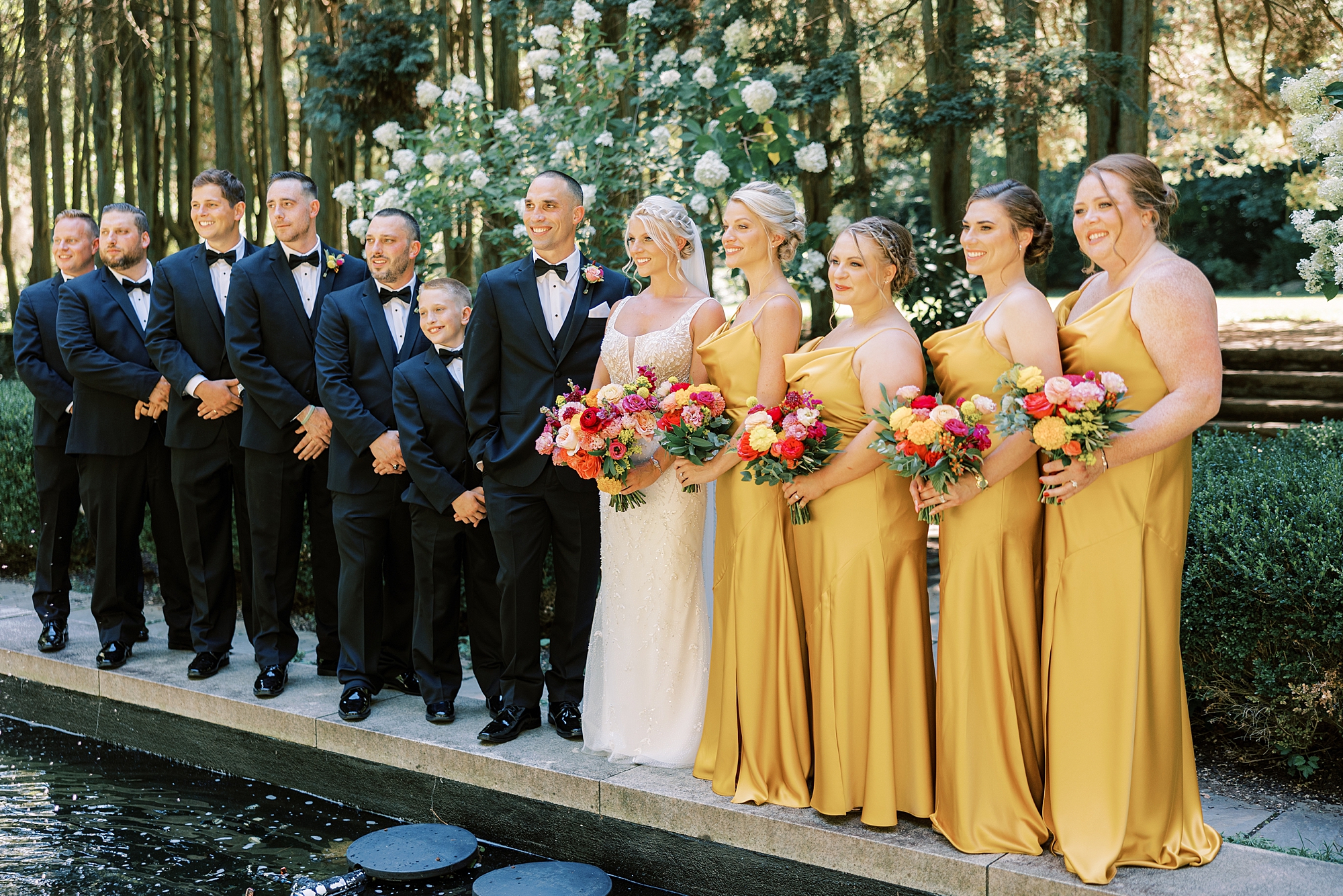wedding party in gold and black attire stands on edge of pool at Parque Ridley Creek