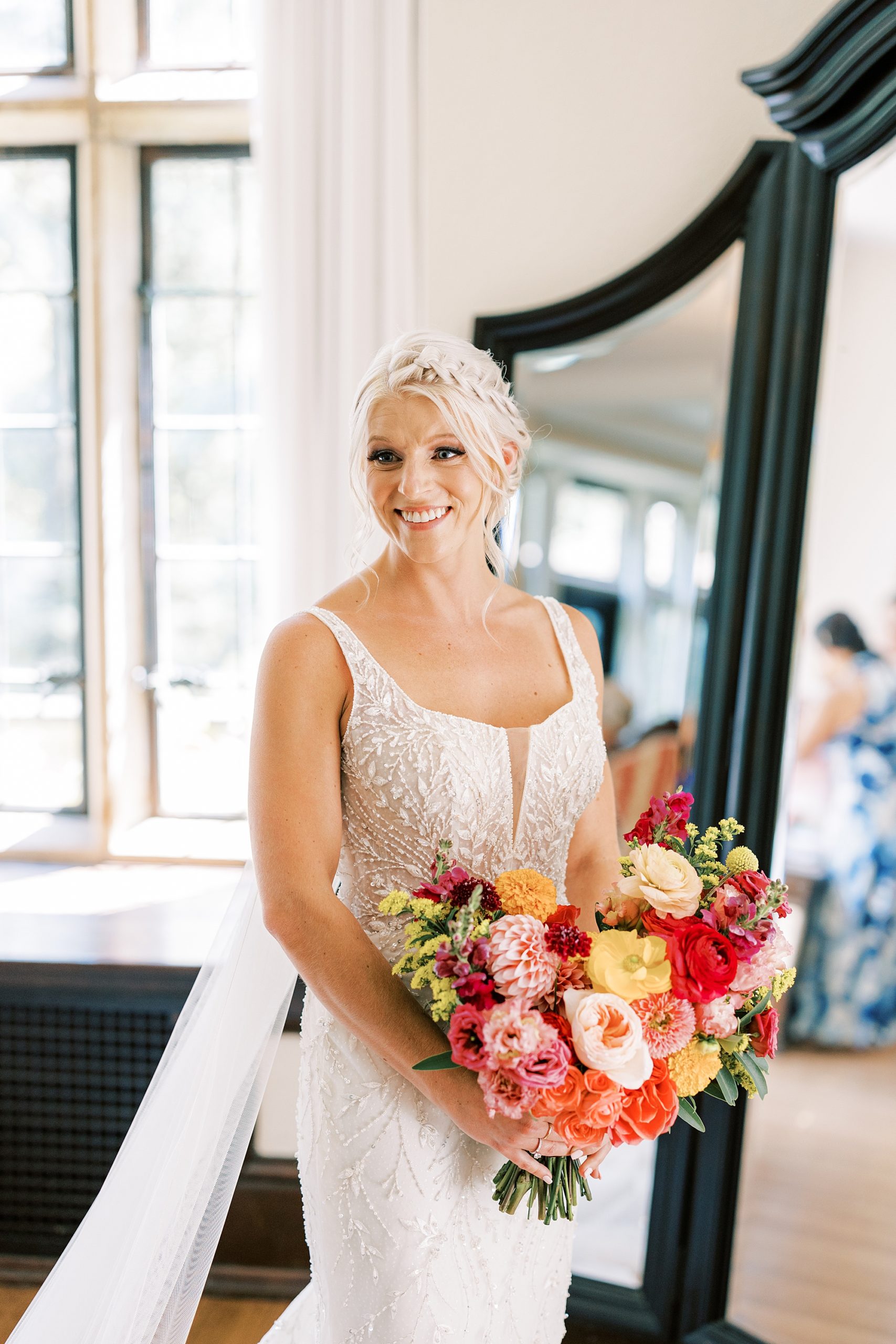 bride stands holding bouquet of bright pink flowers by mirror in suite at Parque Ridley Creek