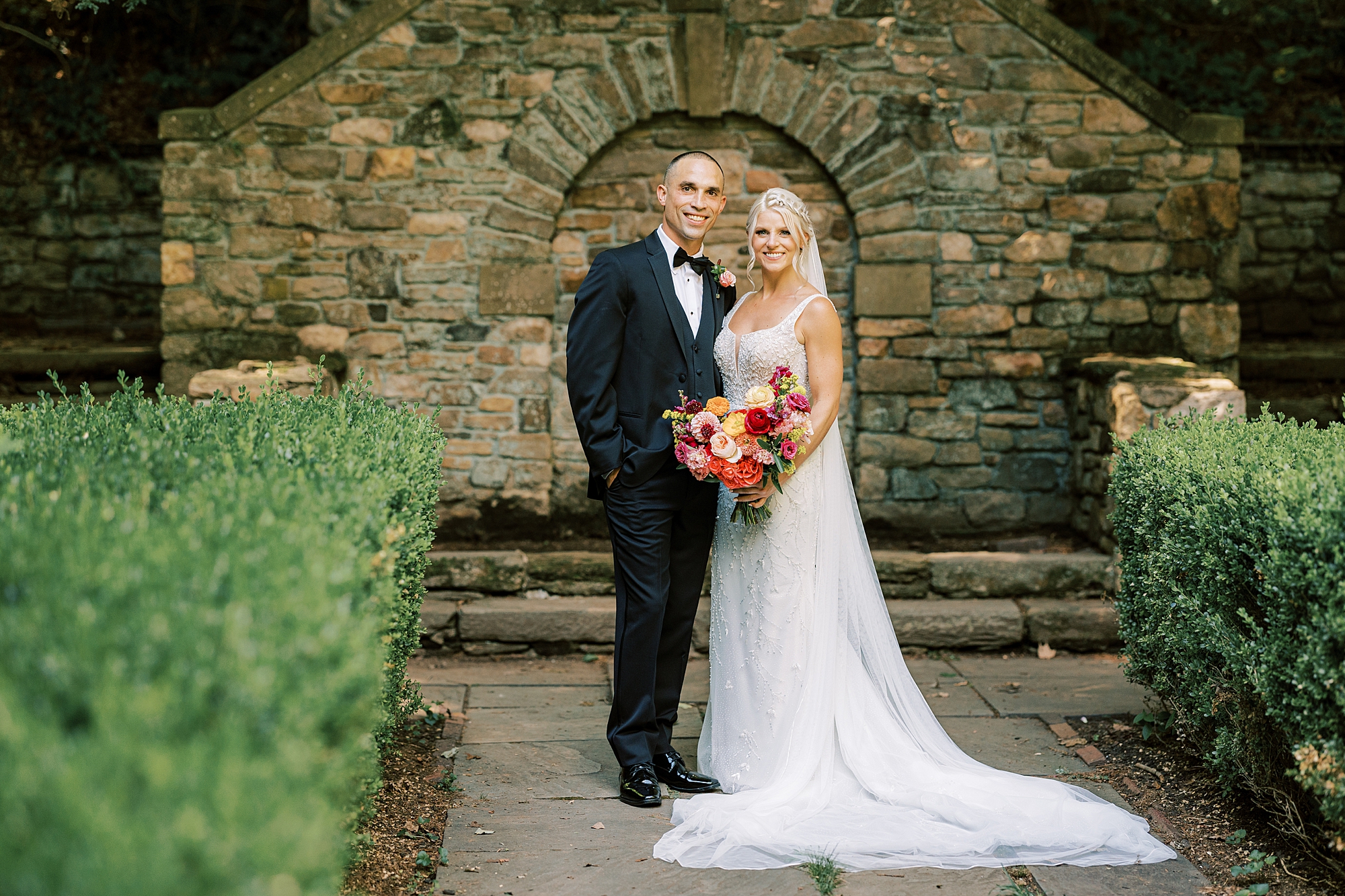 bride and groom pose by stone structure in gardens at Parque Ridley Creek