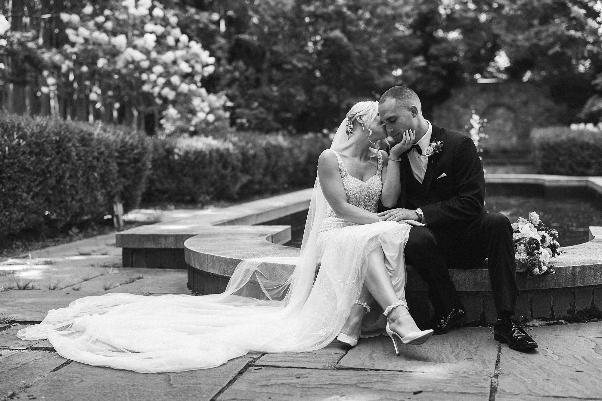 black and white portrait of bride and groom sitting by fountain at Parque Ridley Creek