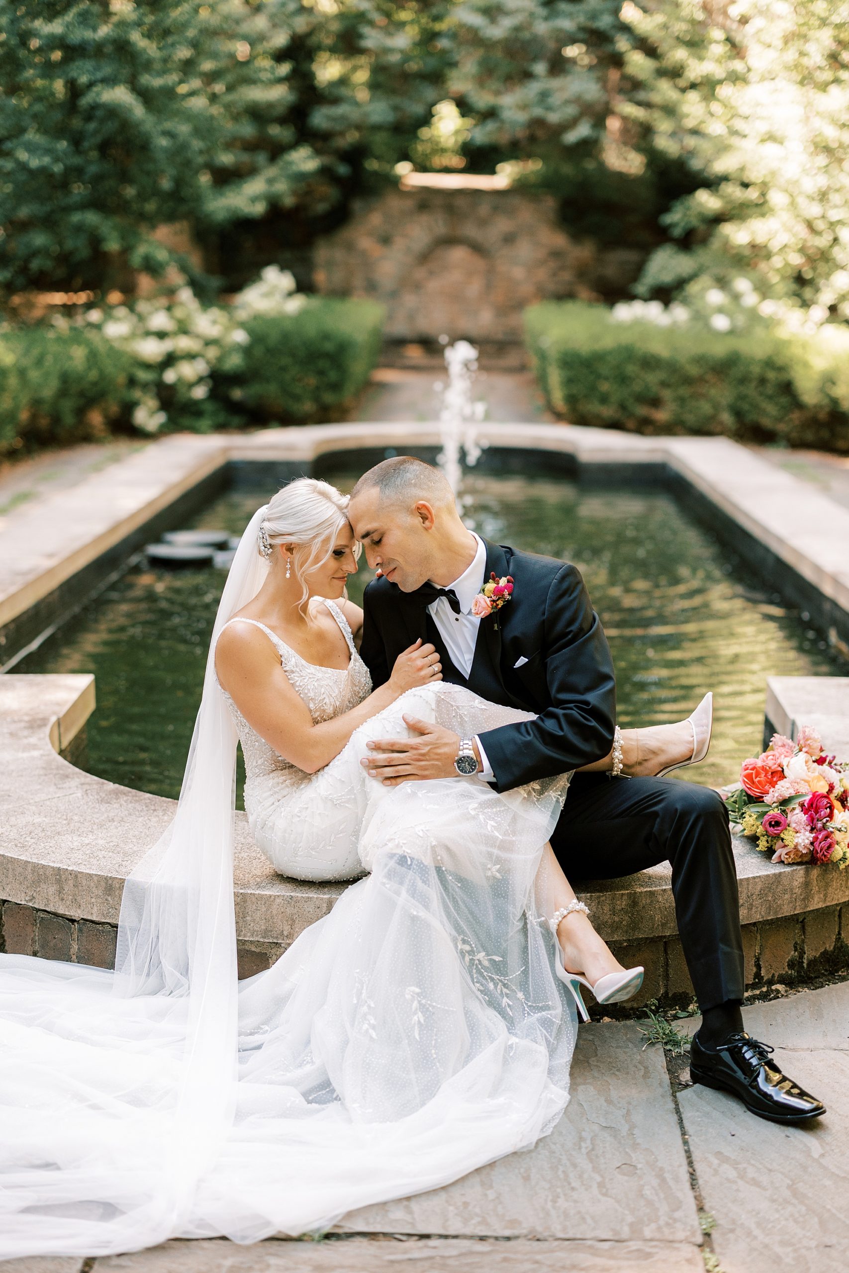 groom holds bride with legs in his lap on edge of pond at Parque Ridley Creek
