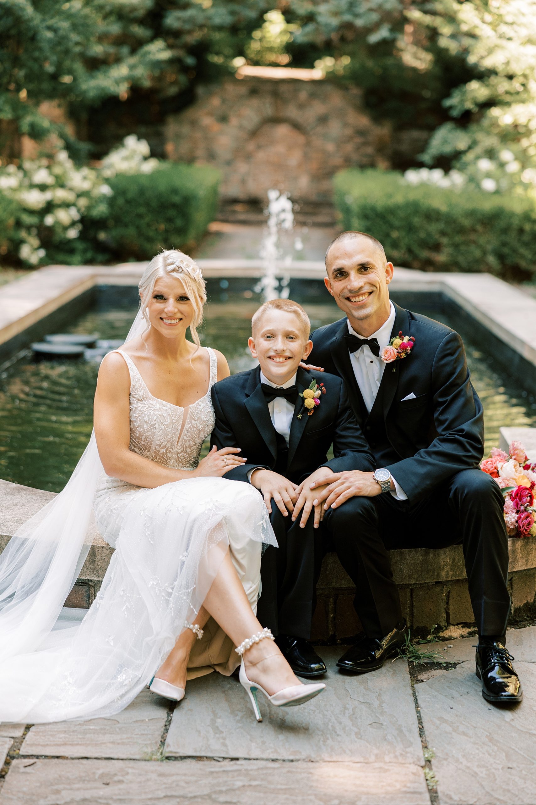 bride and groom sit with son by fountain at Parque Ridley Creek