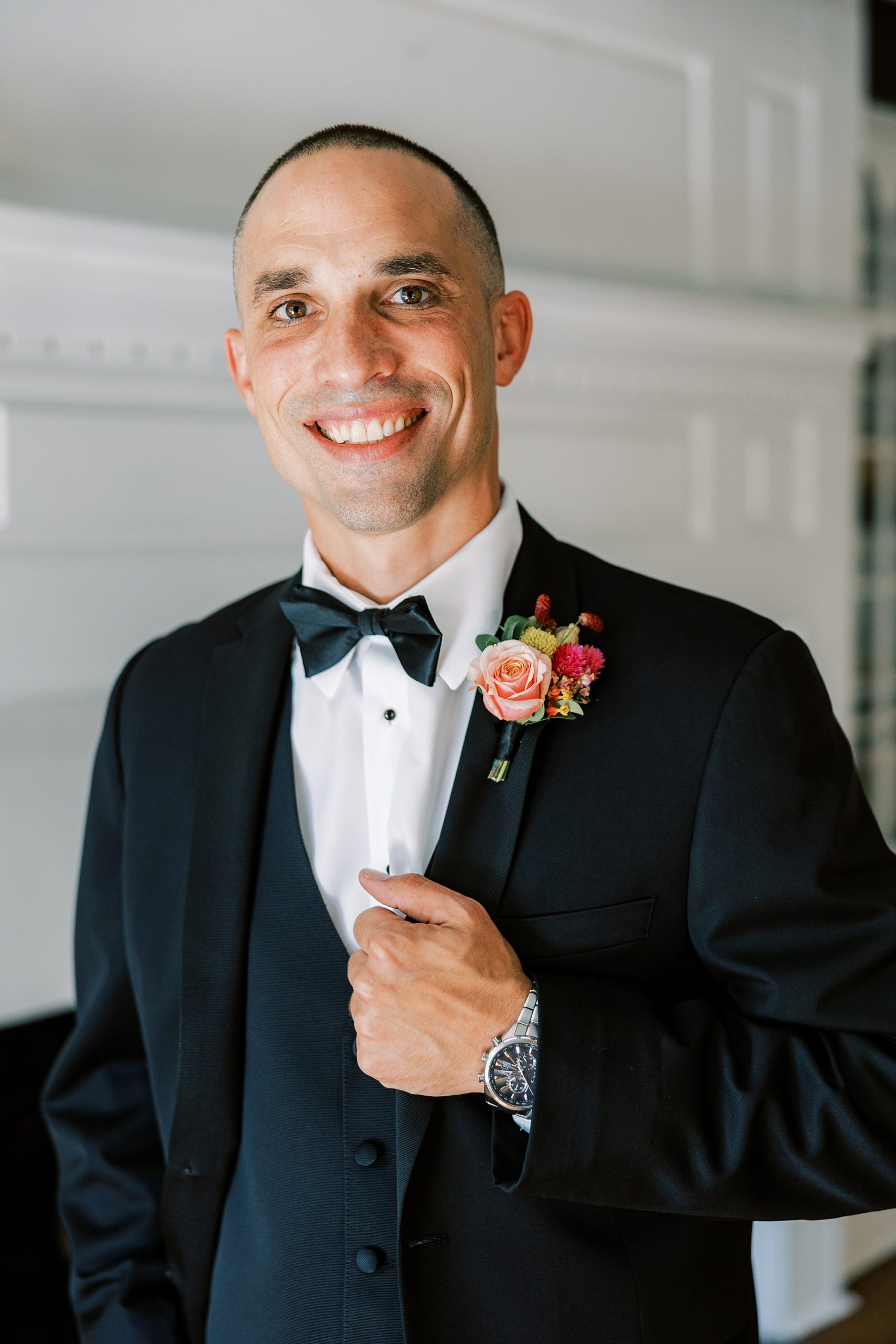 groom adjusts lapel showing off pink and peach boutonnière 