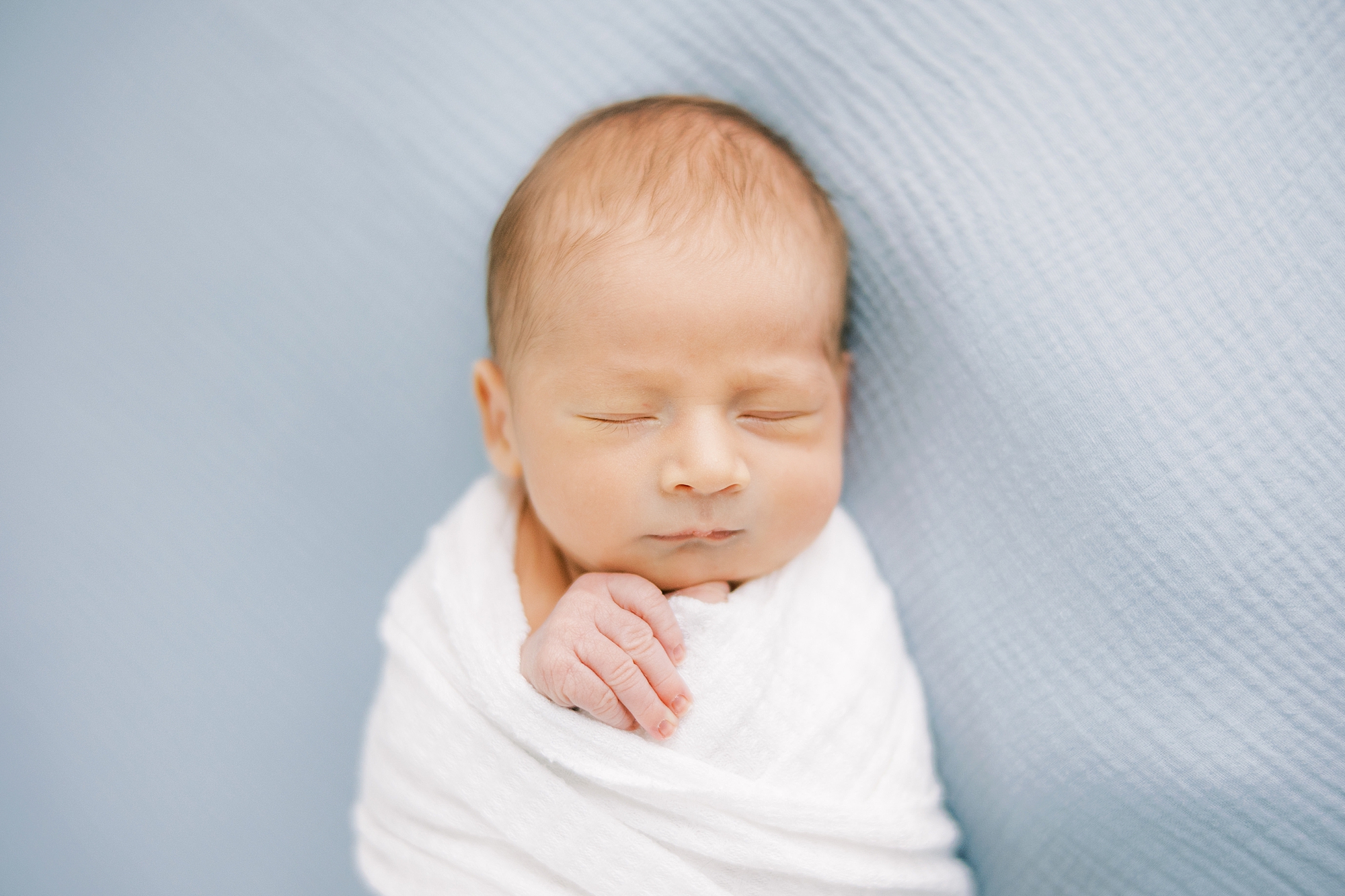 baby boy lays in white wrap on blue blanket 