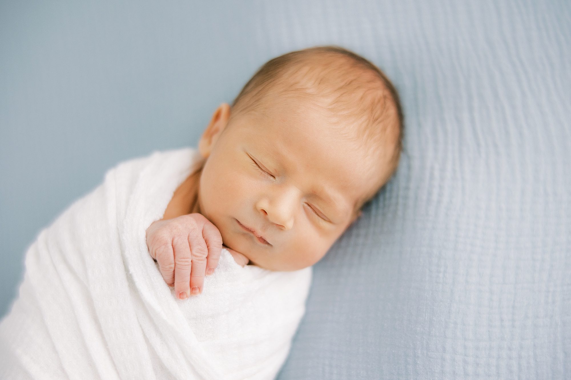 baby boy in white wrap lays on blue blanket during in-home newborn portraits