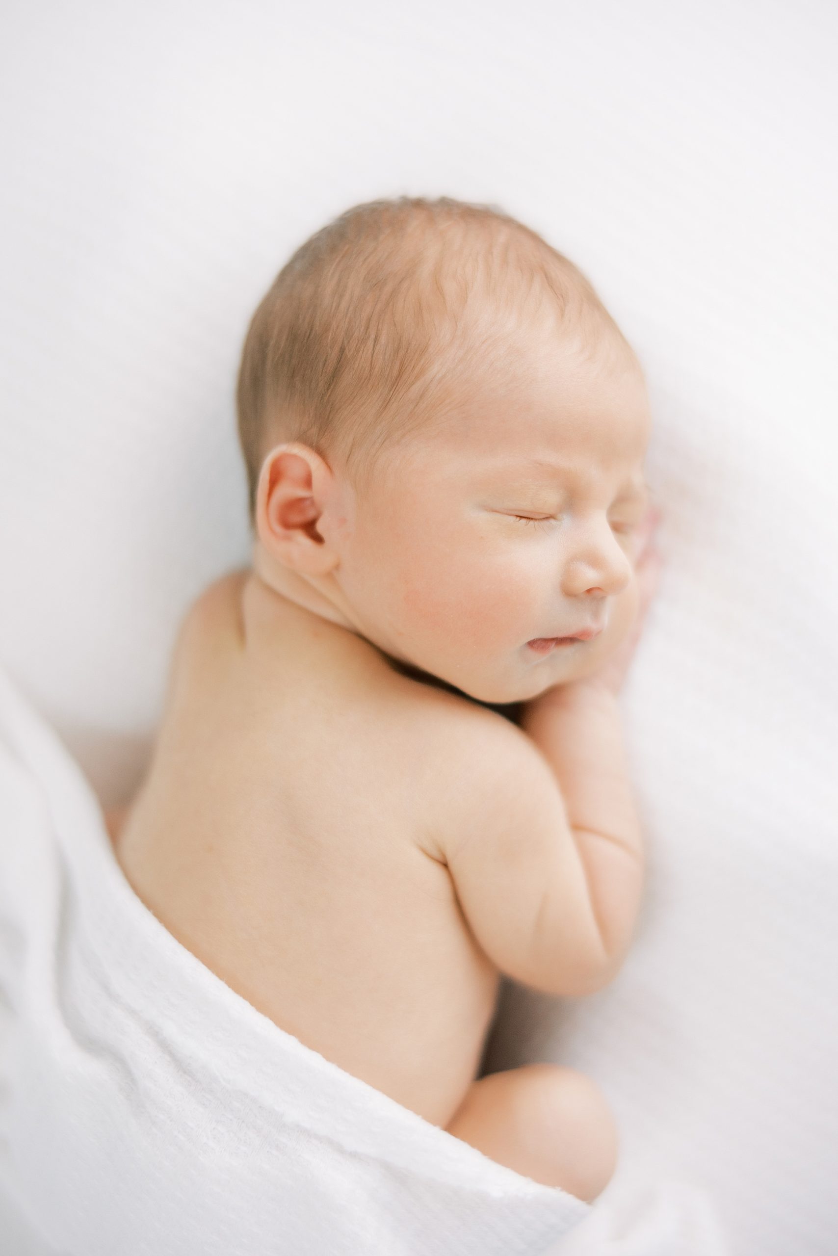 baby sleeps on white blanket during in-home newborn portraits