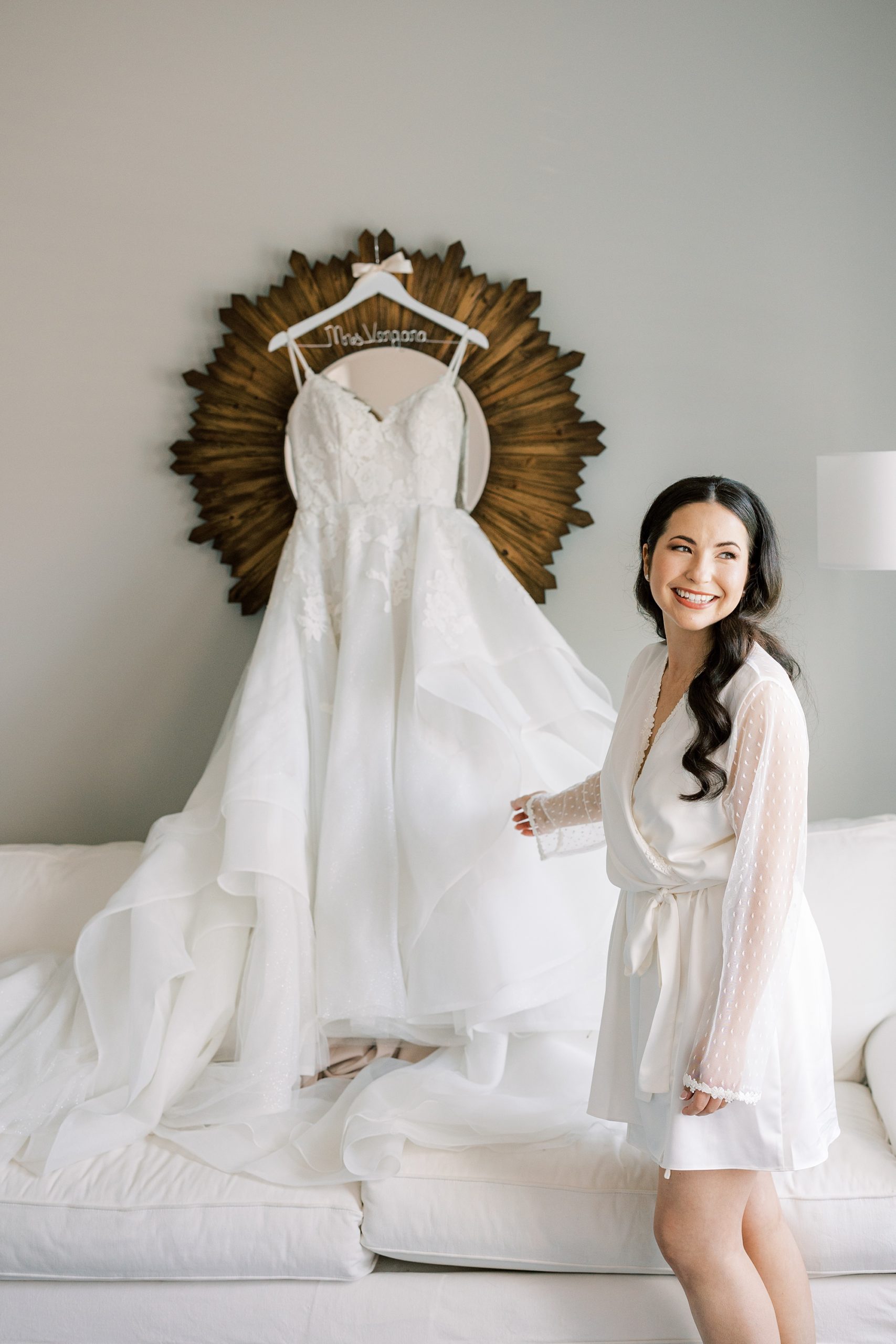 bride smiles looking at wedding dress hanging on mirror in suite at French Creek Golf Club