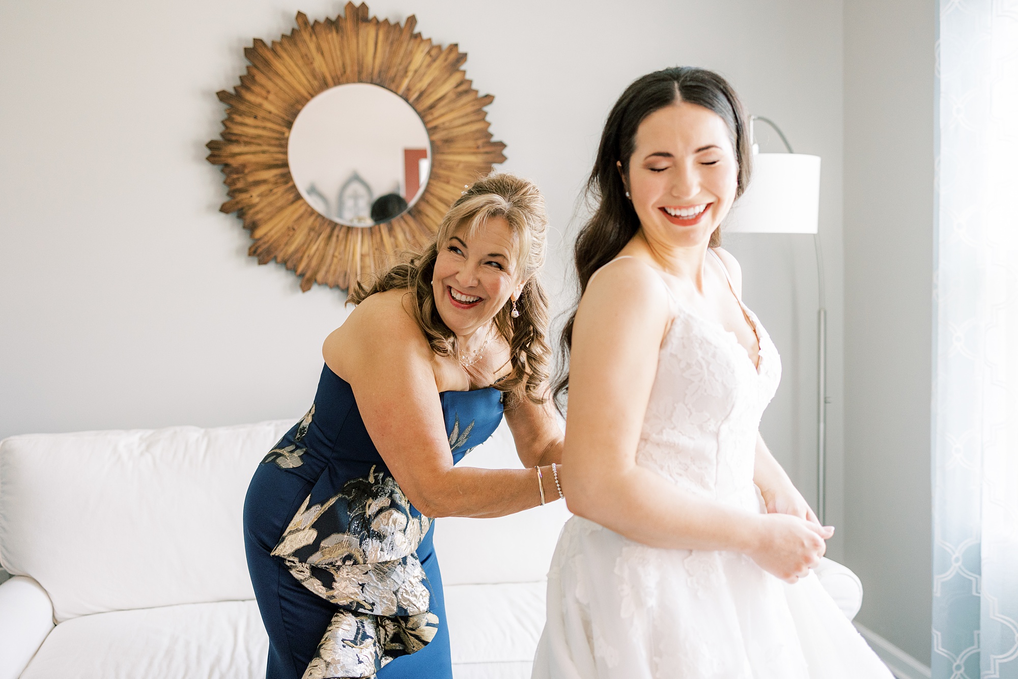 mother in blue dress helps bride into wedding dress