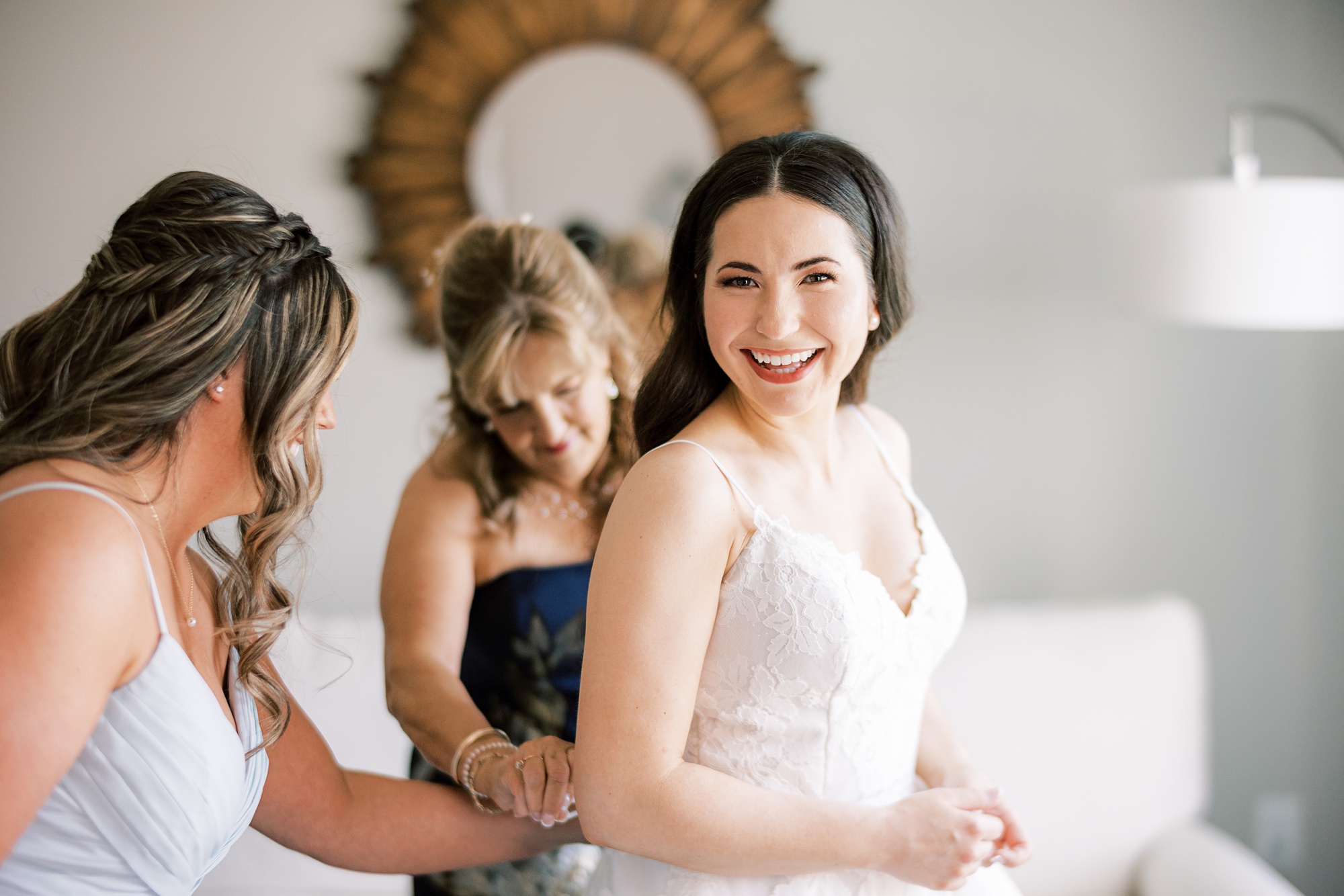 mother and bridesmaid help bride into wedding gown in bridal suite at French Creek Golf Club