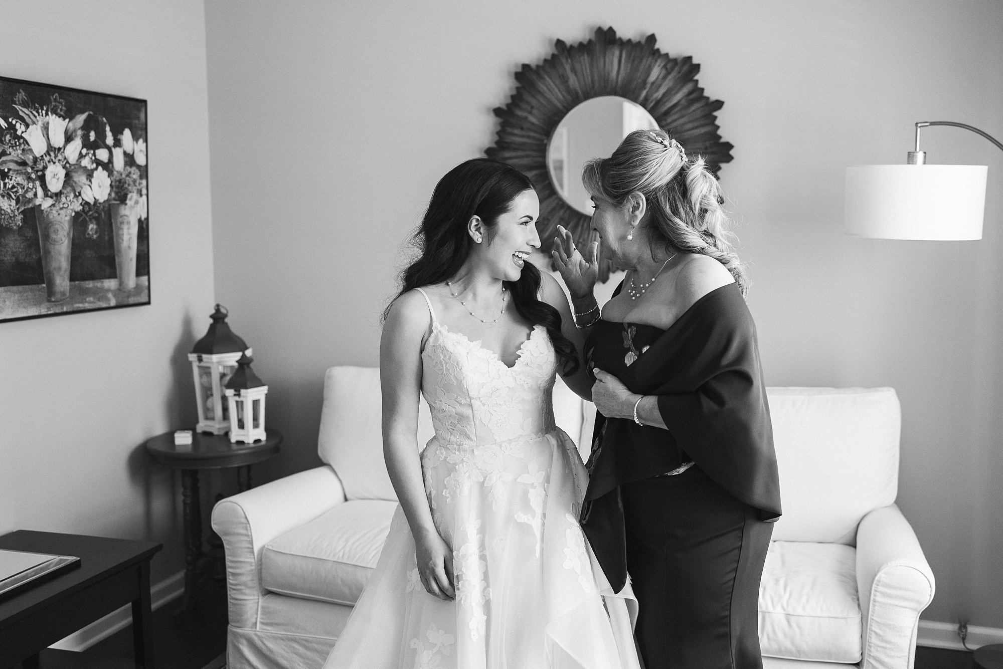 mother and bride hug and smile by mirror in bridal suite 
