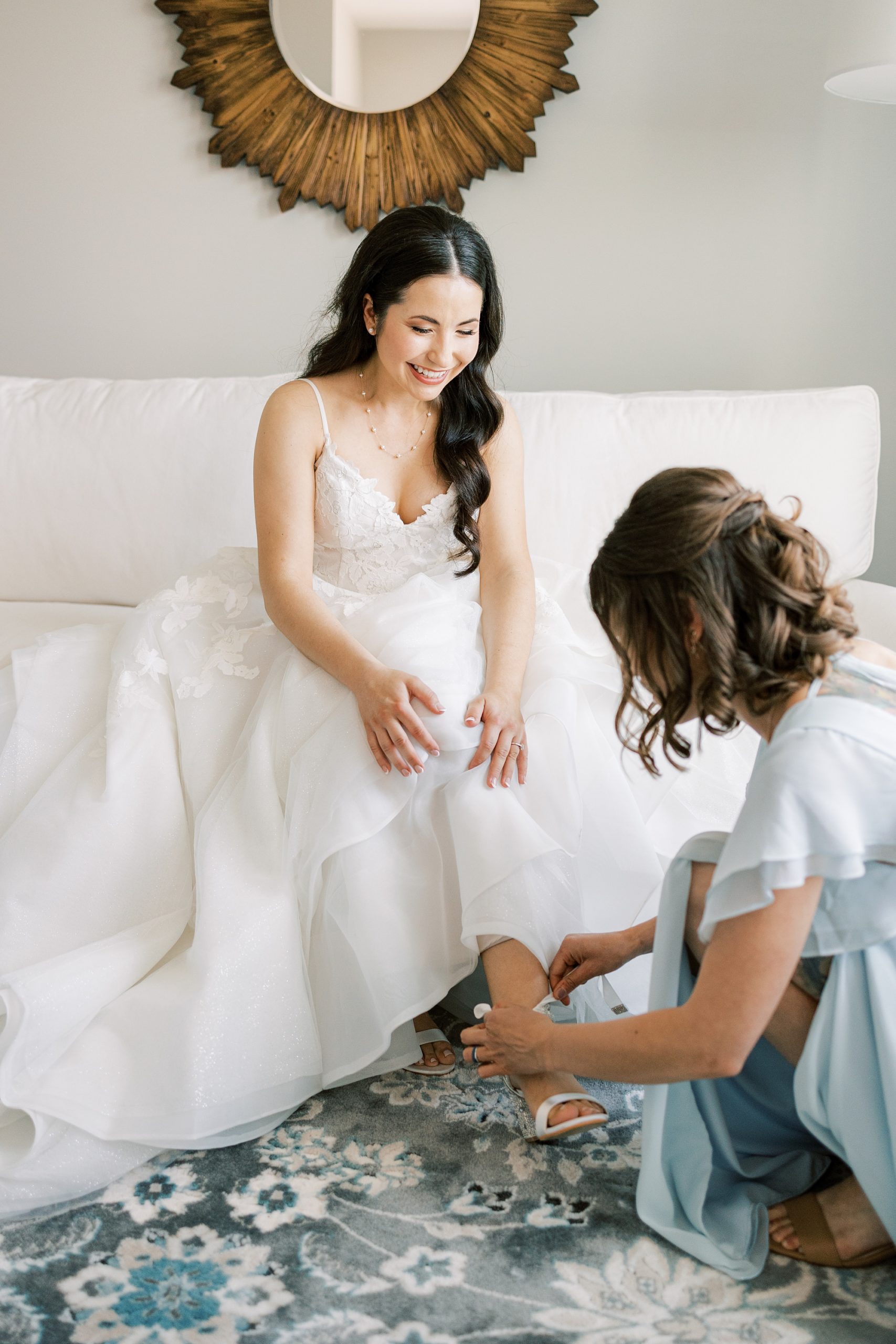 bridesmaid helps bride into shoes on morning of wedding 