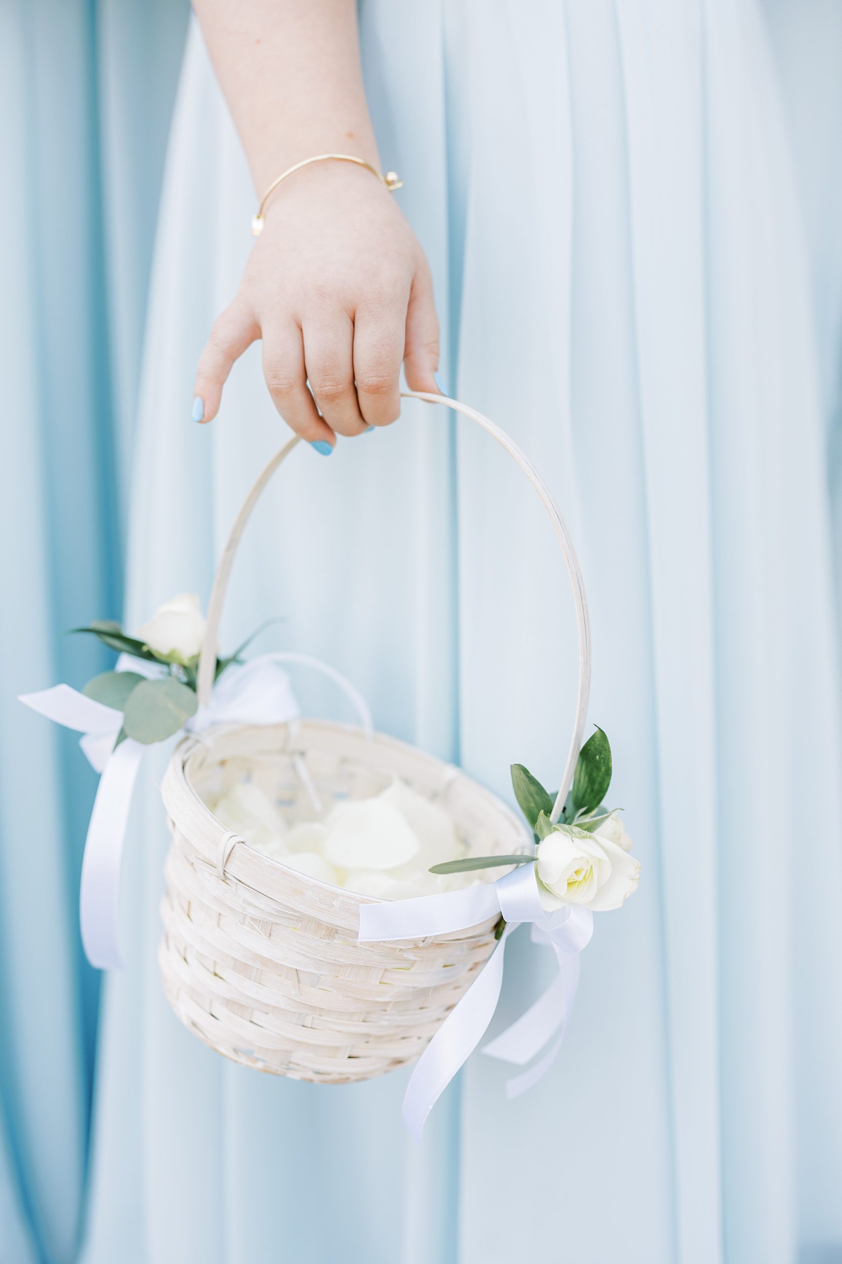 flower girl holds white basket against blue dress