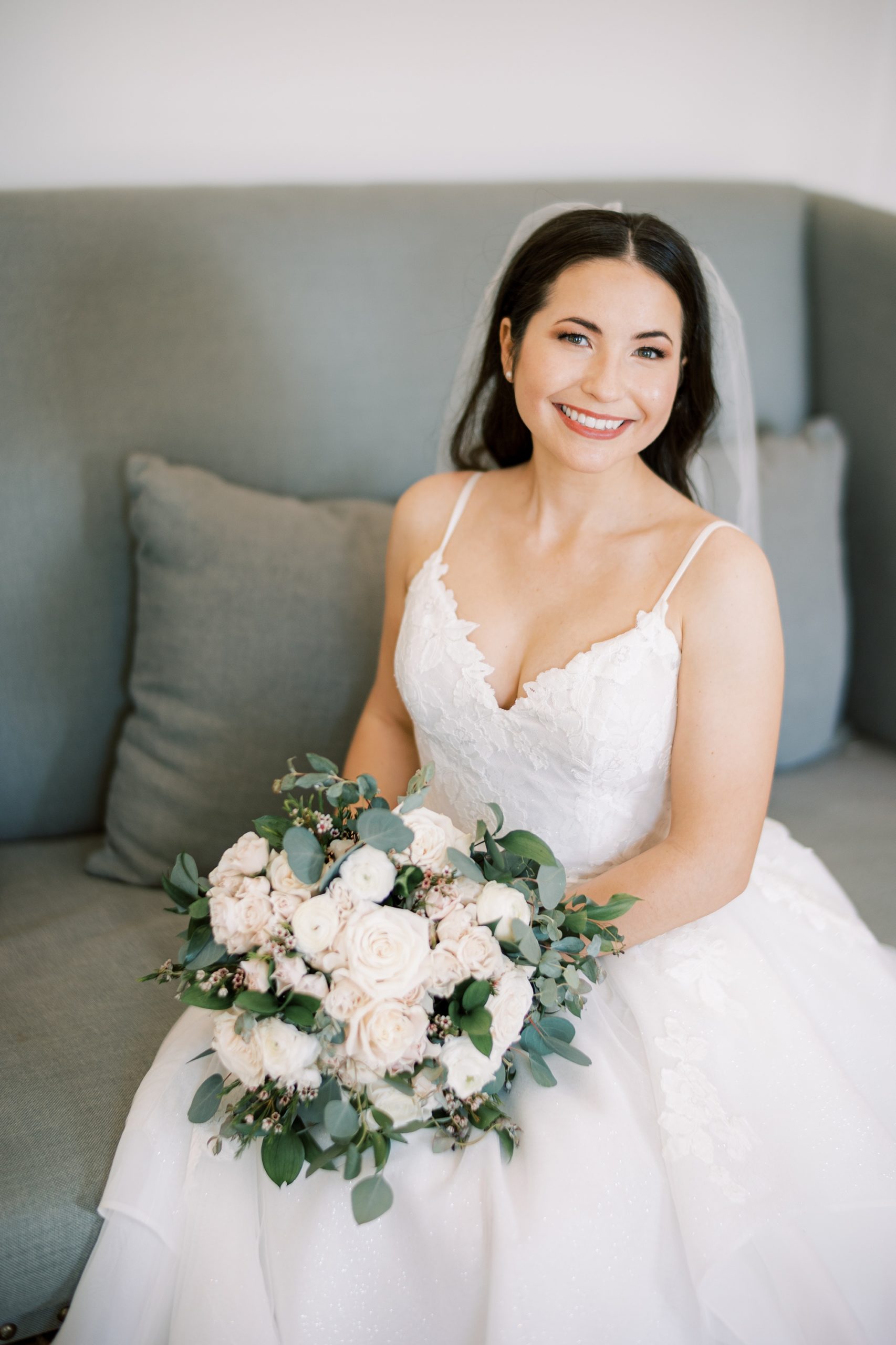 bride sits holding all-white bouquet on couch at French Creek Golf Club
