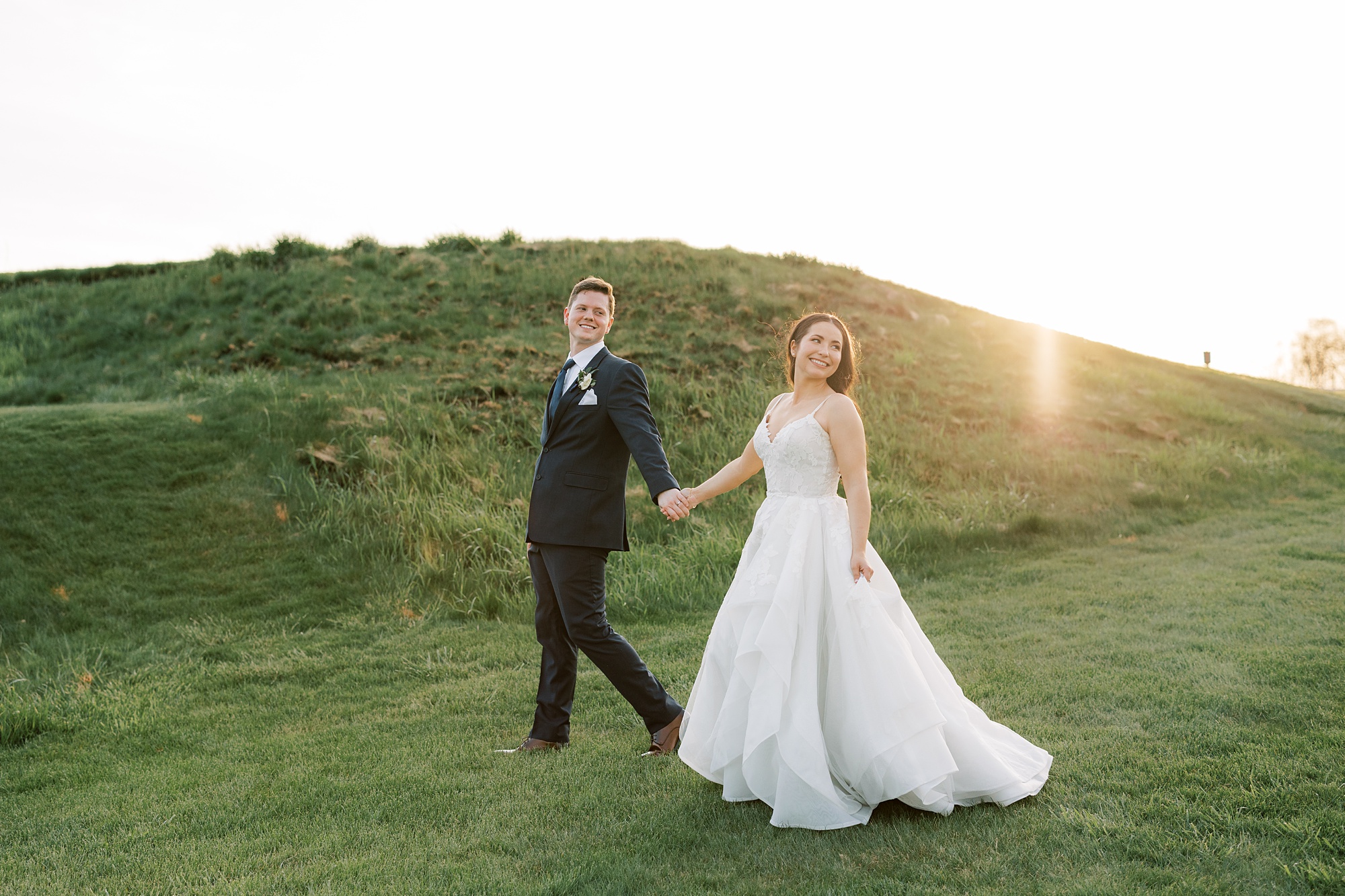 bride and groom hold hands walking on hills at French Creek Golf Club 