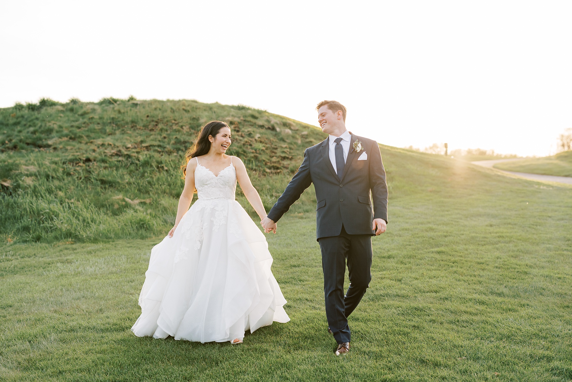 newlyweds hold hands walking on hill at French Creek Golf Club