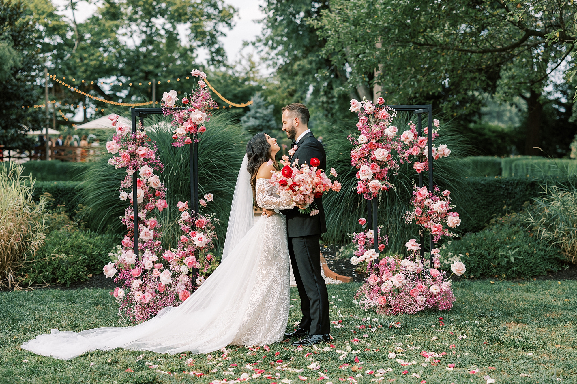 bride and groom hug between pink and white floral display 