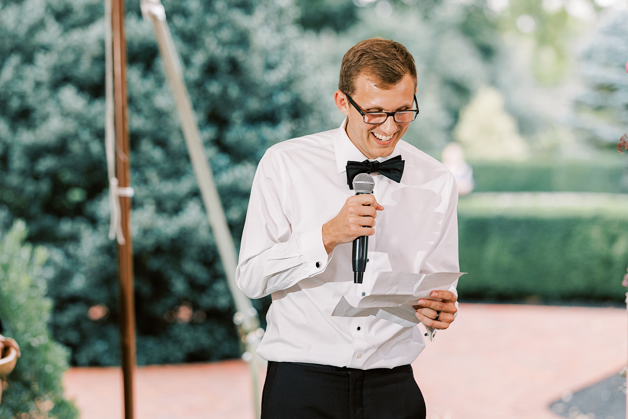 groomsman in white shirt with bow tie reads speech 