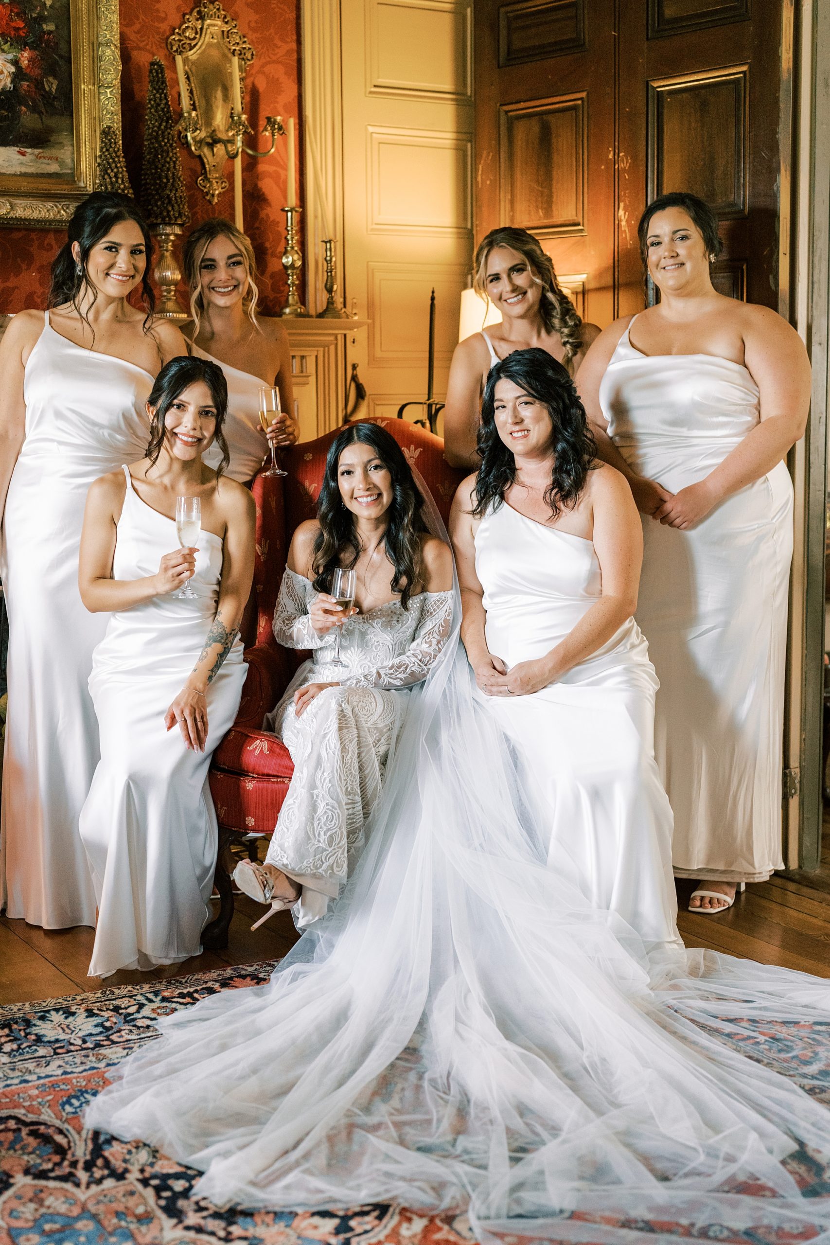 bride sits with bridesmaids in white gowns in suite at The Cypress House