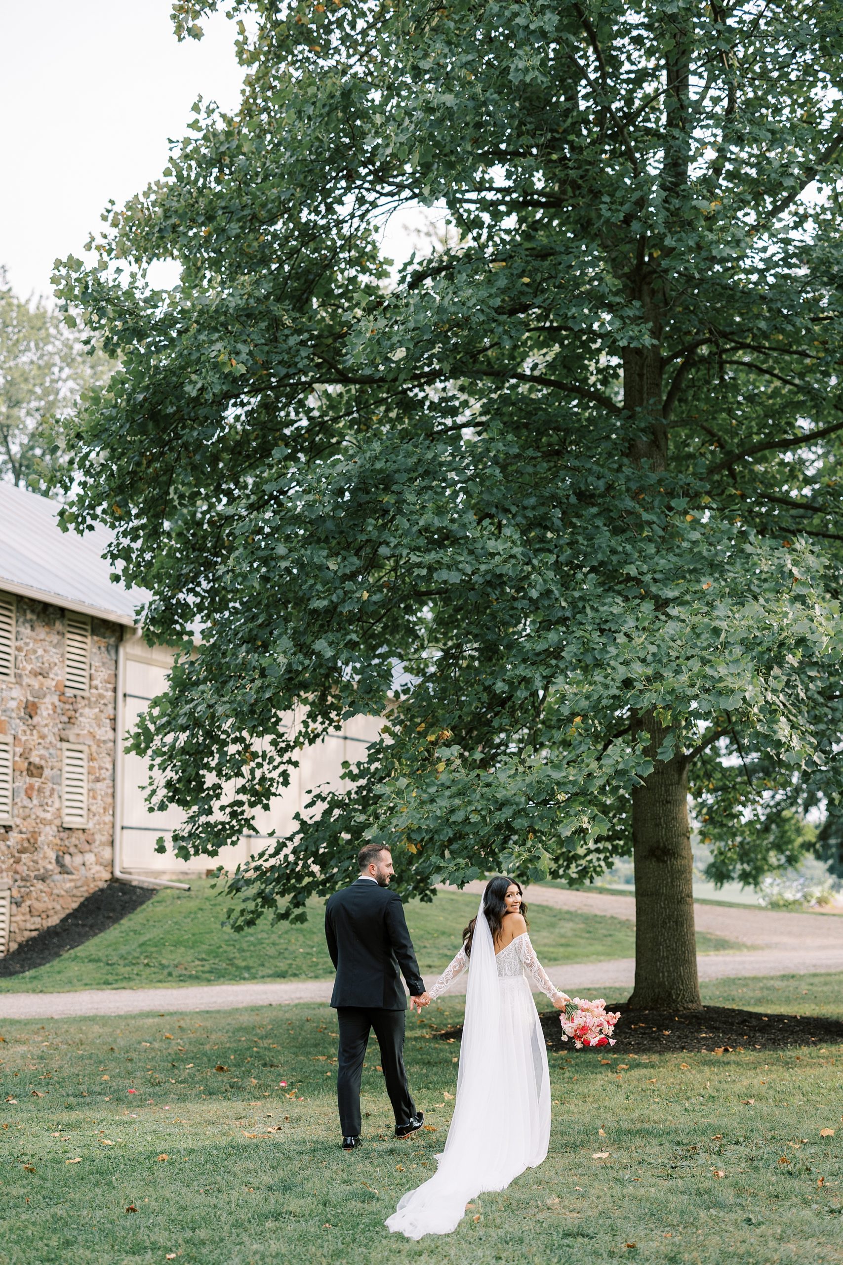 newlyweds walk under trees near stone building at The Cypress House