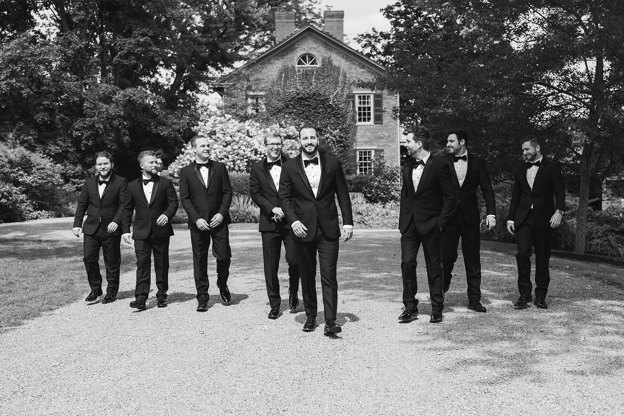 groom and groomsmen walk outside The Cypress House in suits 