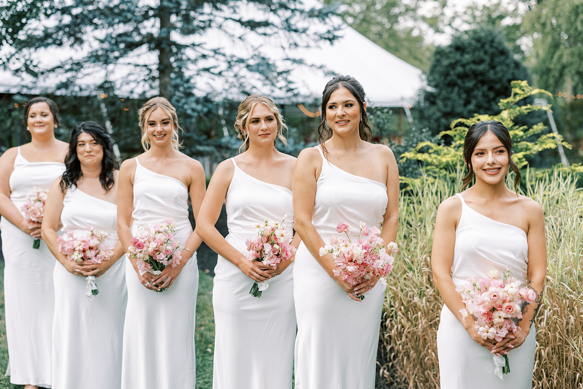 bridesmaids in white gowns hold pink bouquets during ceremony 