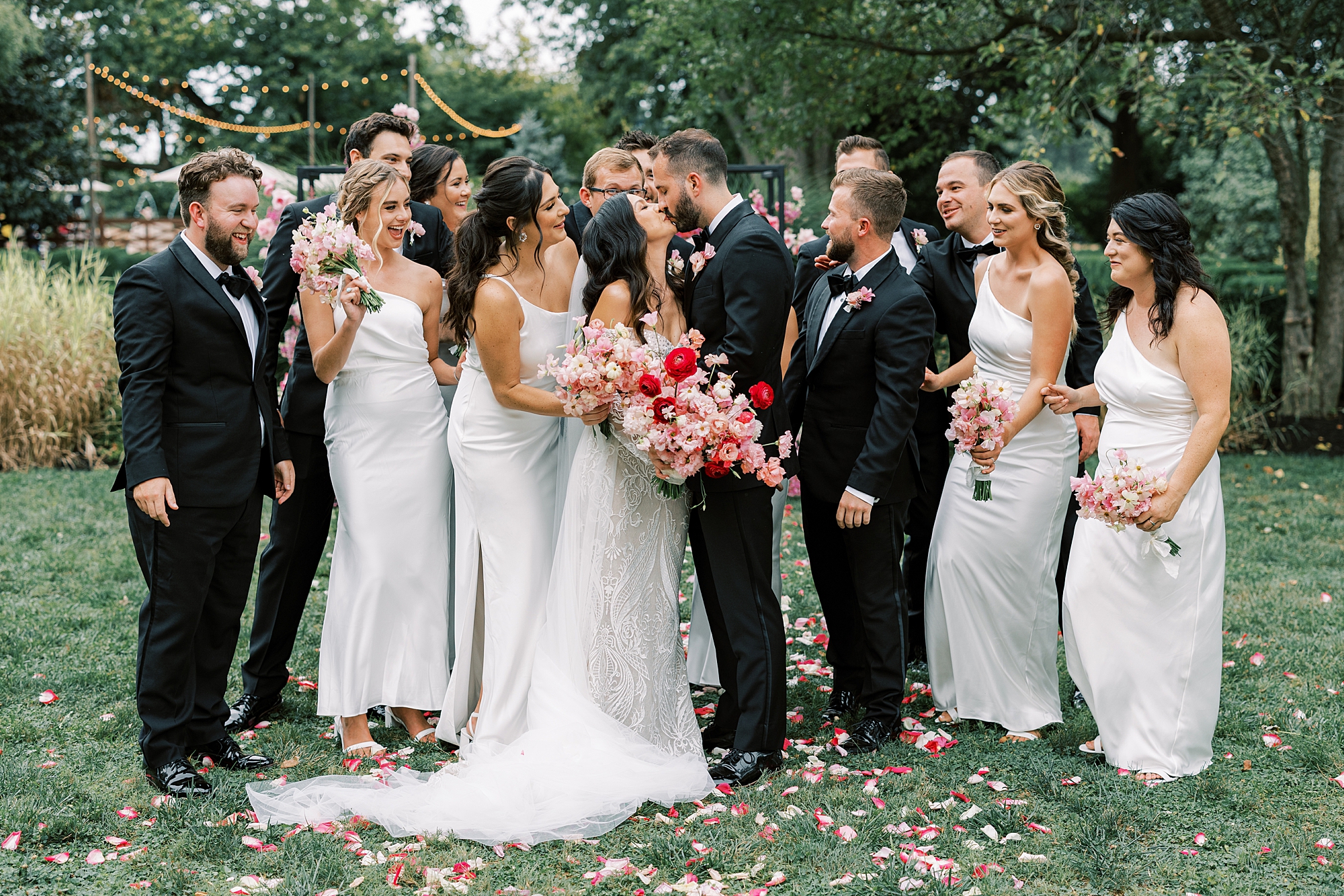 bride and groom kiss with wedding party around them cheering 