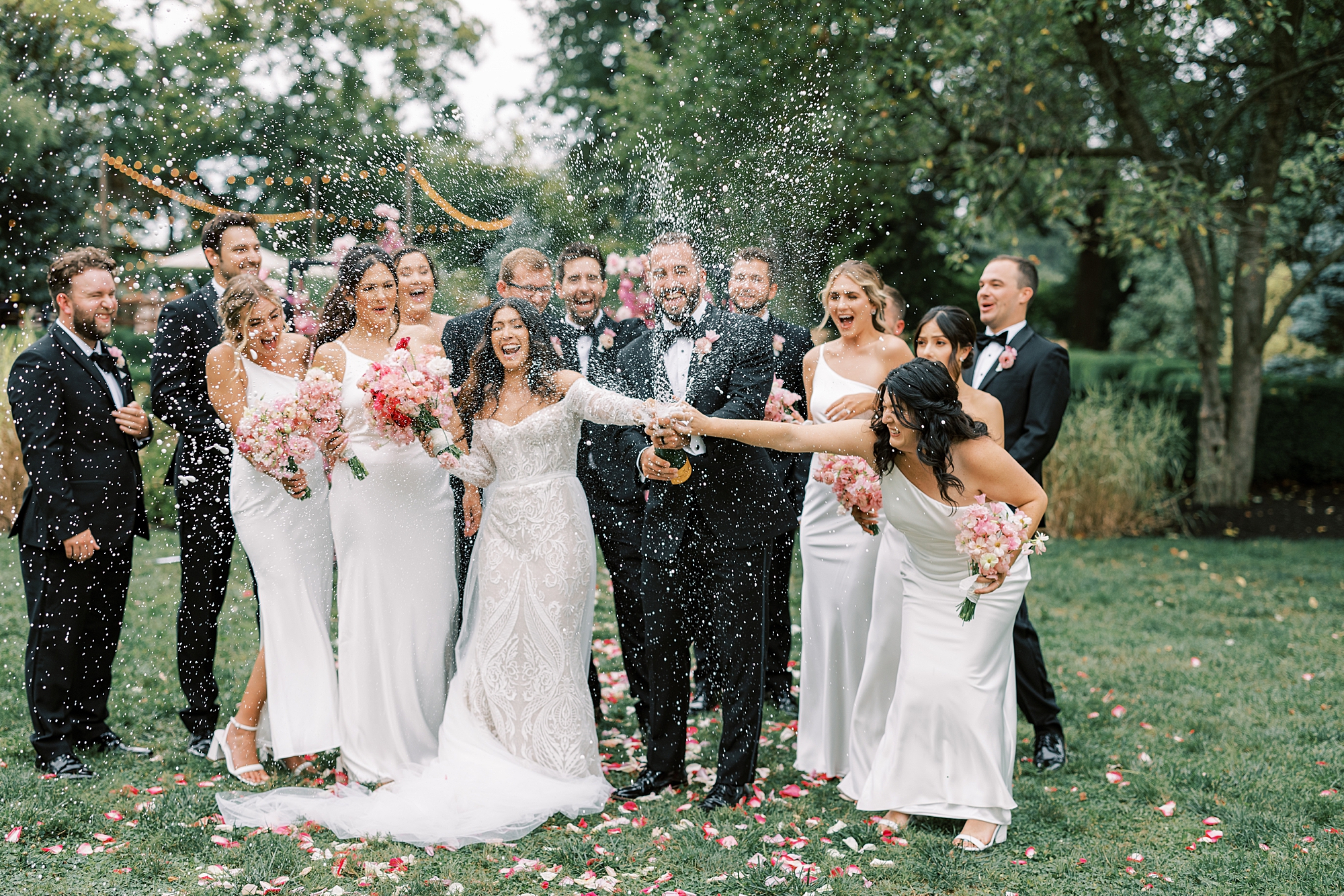 bride holds bridesmaids hand while groom pops champagne 